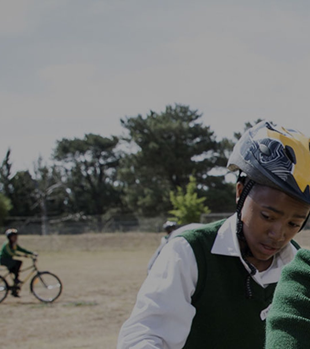 {generated} 學生佩戴頭盔在戶外騎行，在山景背景中參與Breitling x Qhubeka公益活動。