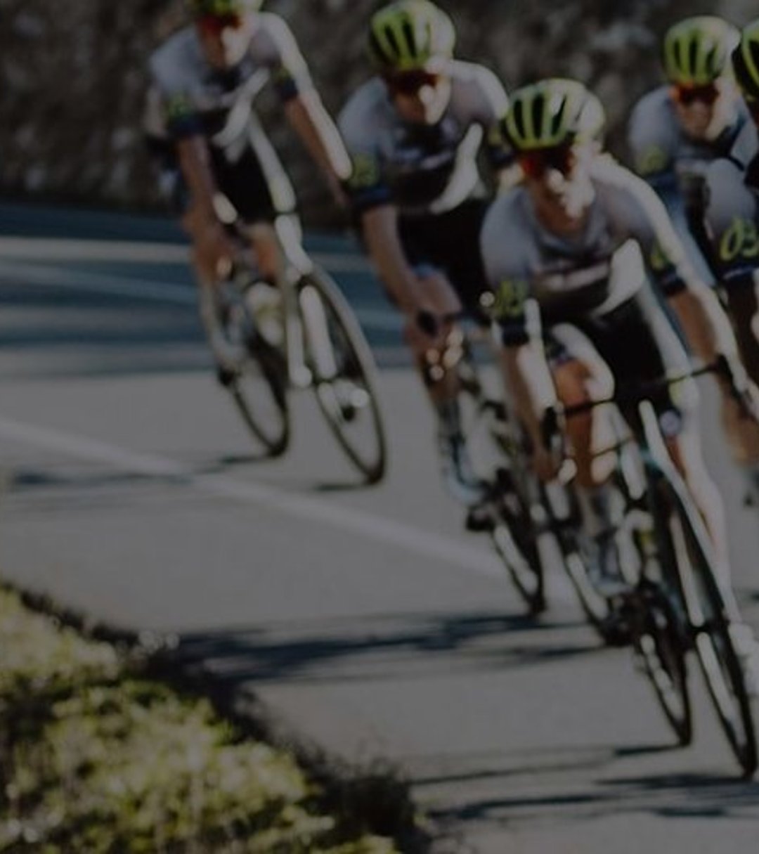 {generated} Cyclists in coordinated team kits with visible Breitling branding ride in formation along a curving sunlit road.
