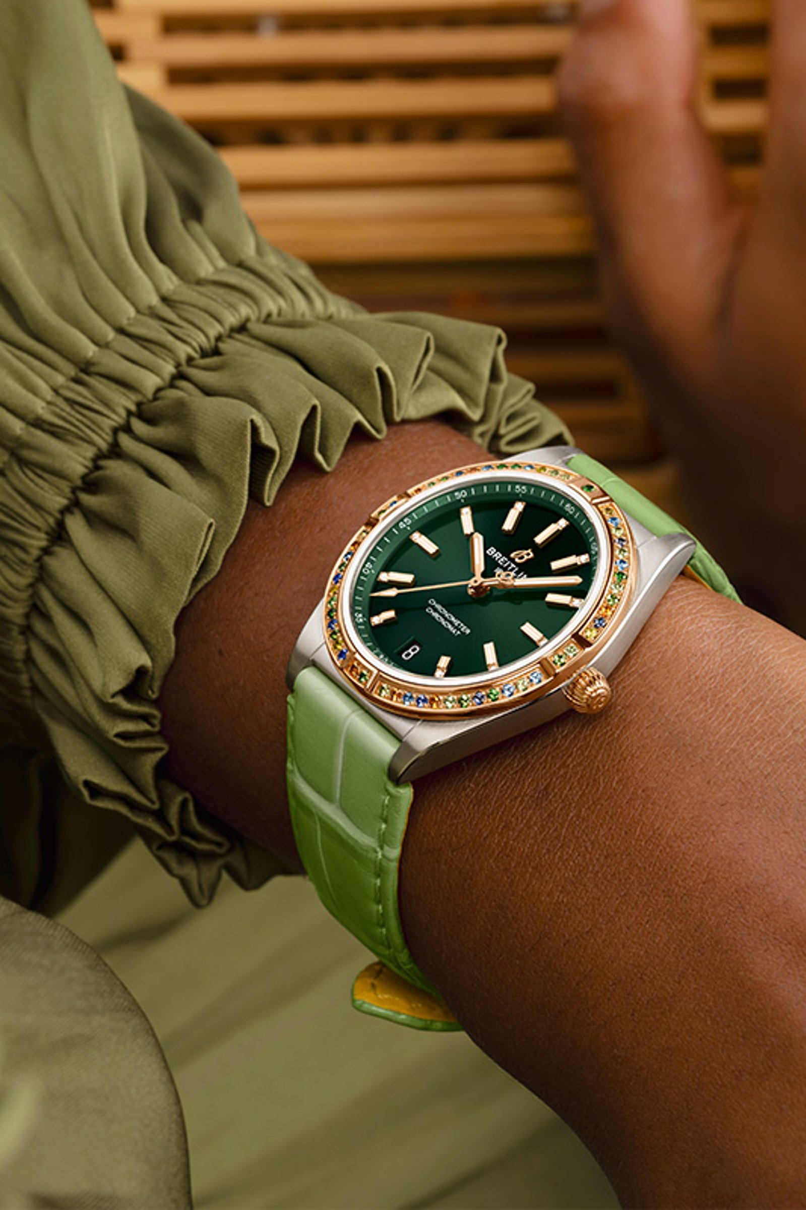 {generated} Ein feminines Handgelenk in Pastelltönen präsentiert eine Breitling Uhr mit grünem Zifferblatt, Edelsteinlünette und passendem Band.