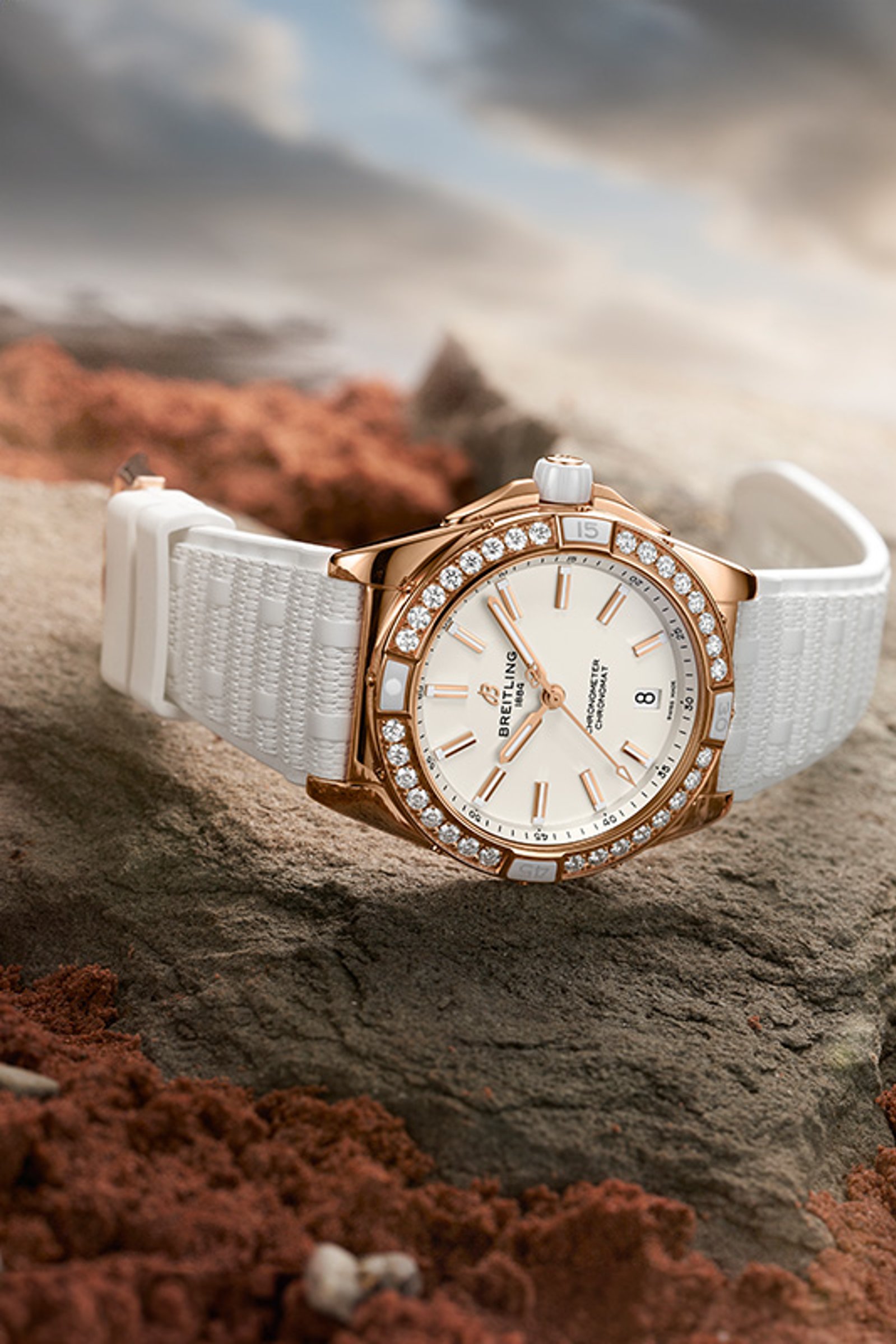 {generated} Breitling Damenuhr in Gold mit Diamantlünette und weißem Armband auf rauem Stein in sanftem, warmem Licht präsentiert.