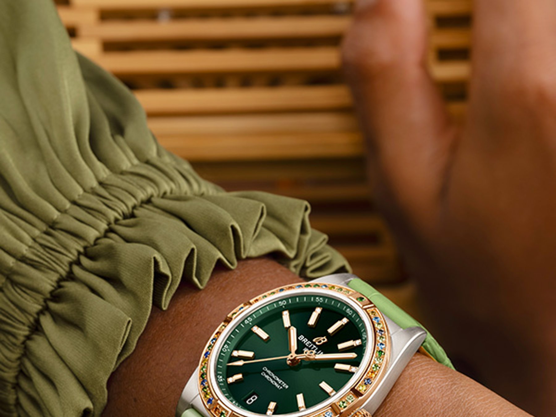 {generated} Ein feminines Handgelenk in Pastelltönen präsentiert eine Breitling Uhr mit grünem Zifferblatt, Edelsteinlünette und passendem Band.