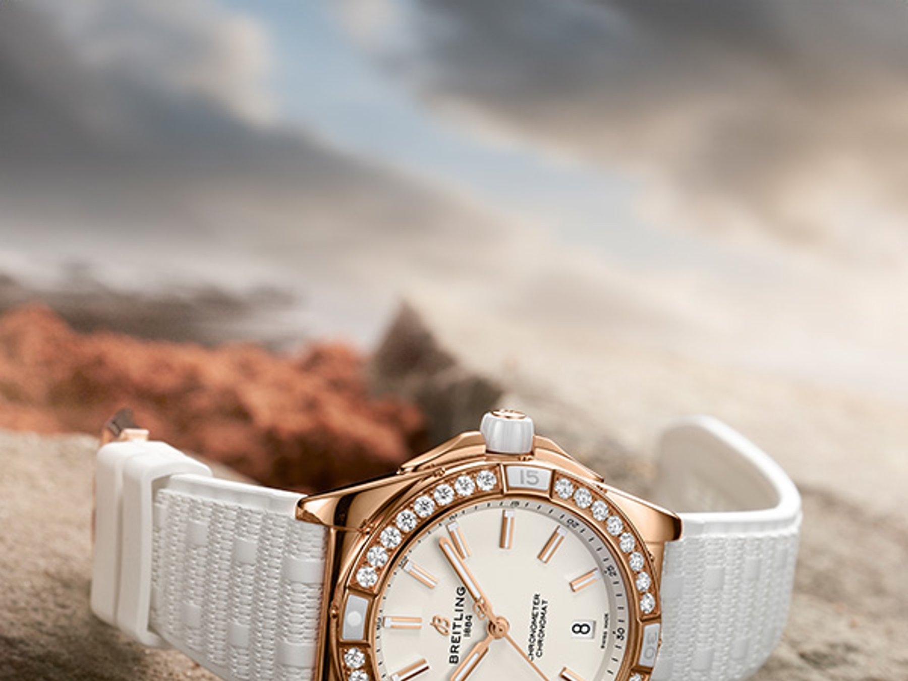 {generated} Breitling Damenuhr in Gold mit Diamantlünette und weißem Armband auf rauem Stein in sanftem, warmem Licht präsentiert.