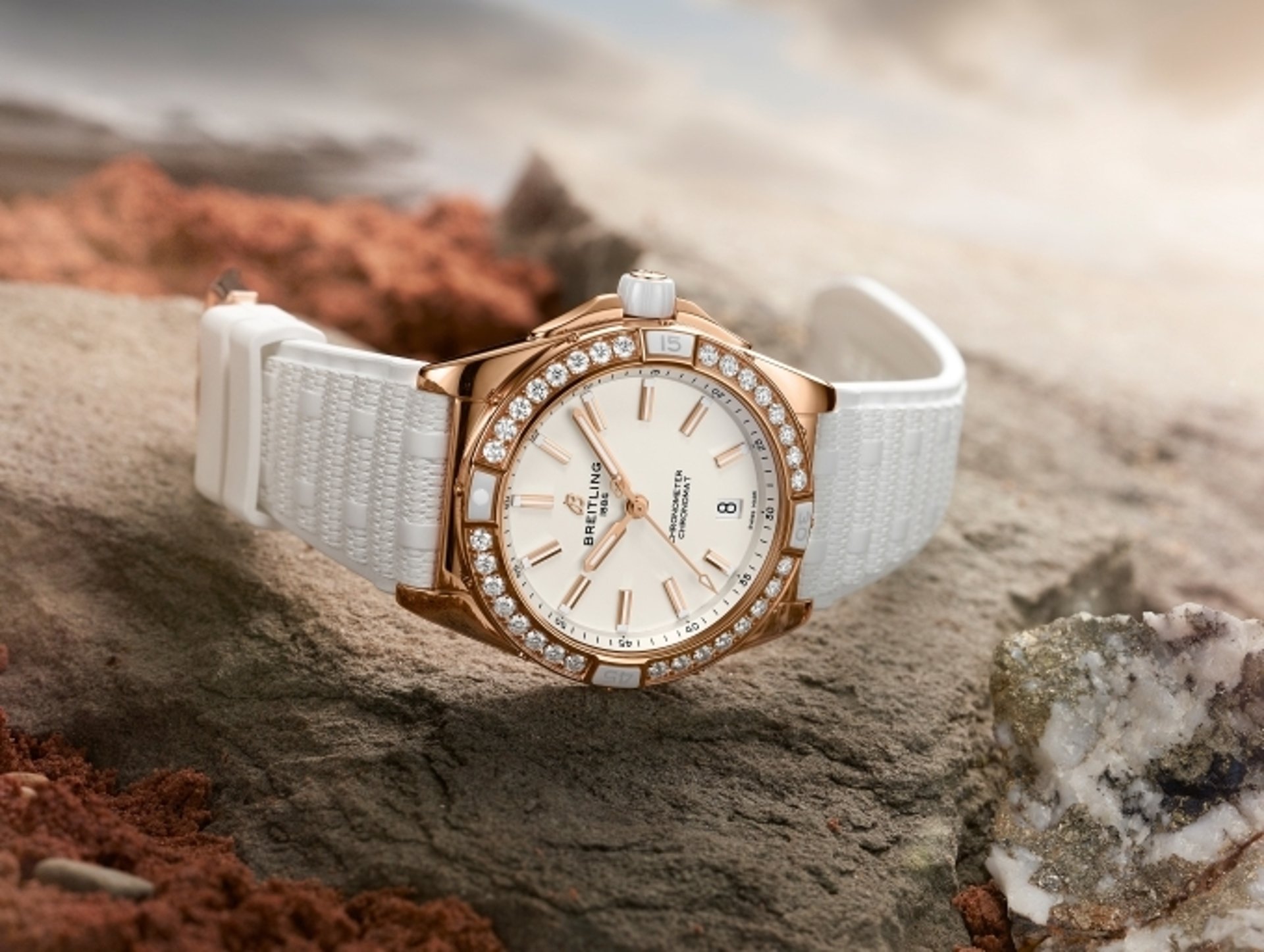 {generated} Breitling Chronomat watch in rose gold with diamond bezel and white strap displayed on rugged stone terrain.