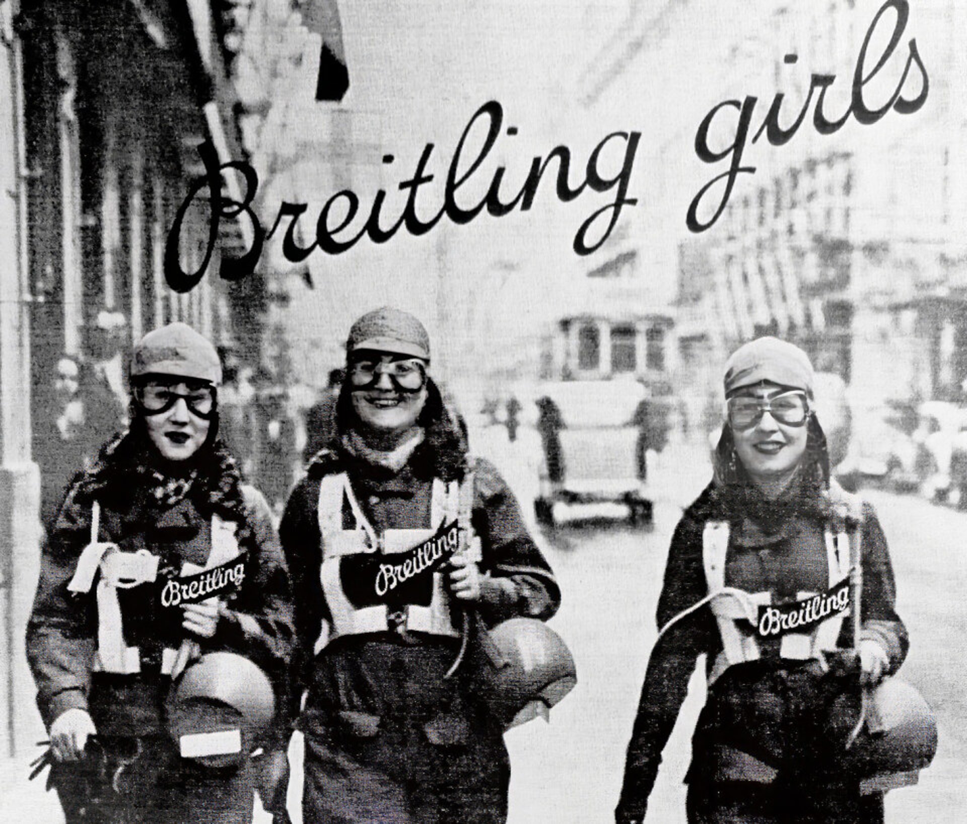 {generated} 三位身著復古航空裝備的女性走在城市街道上，醒目的Breitling標識展現品牌的傳統與風格
