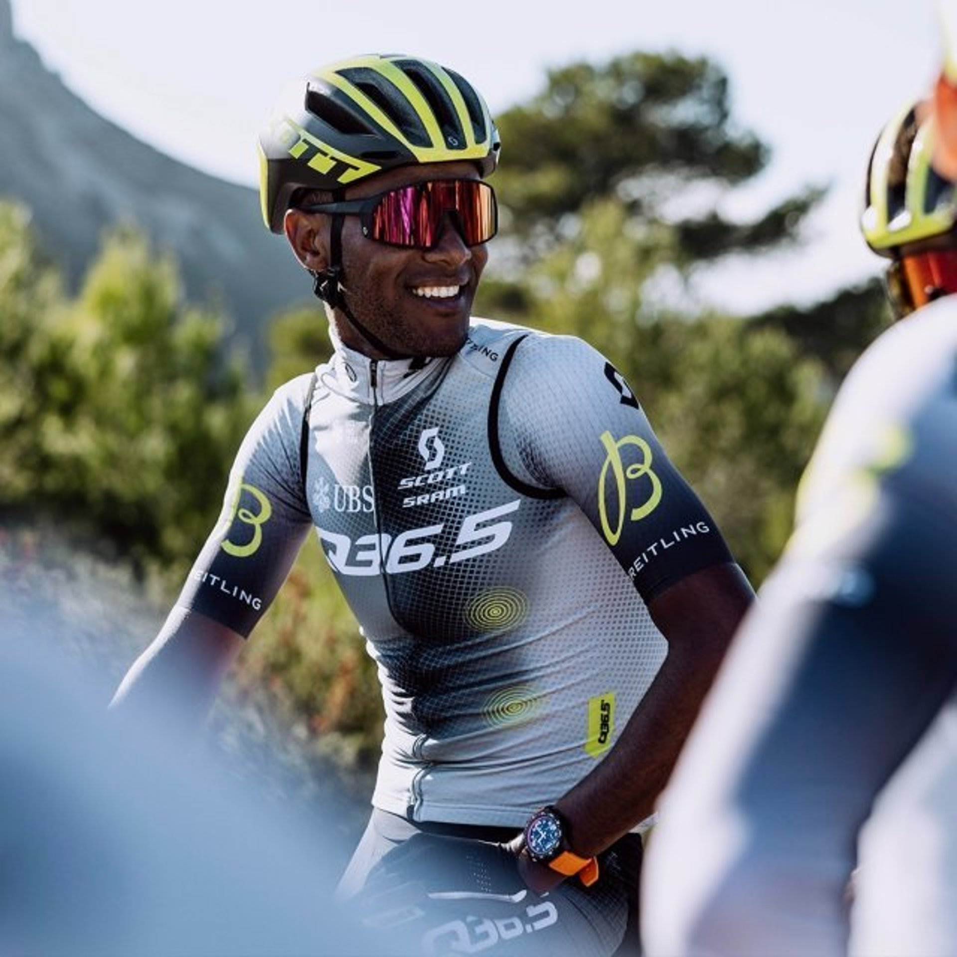 {generated} Cyclist in Q36.5 racing kit and helmet rides outdoors, showcasing a Breitling watch amid a bright, scenic landscape.