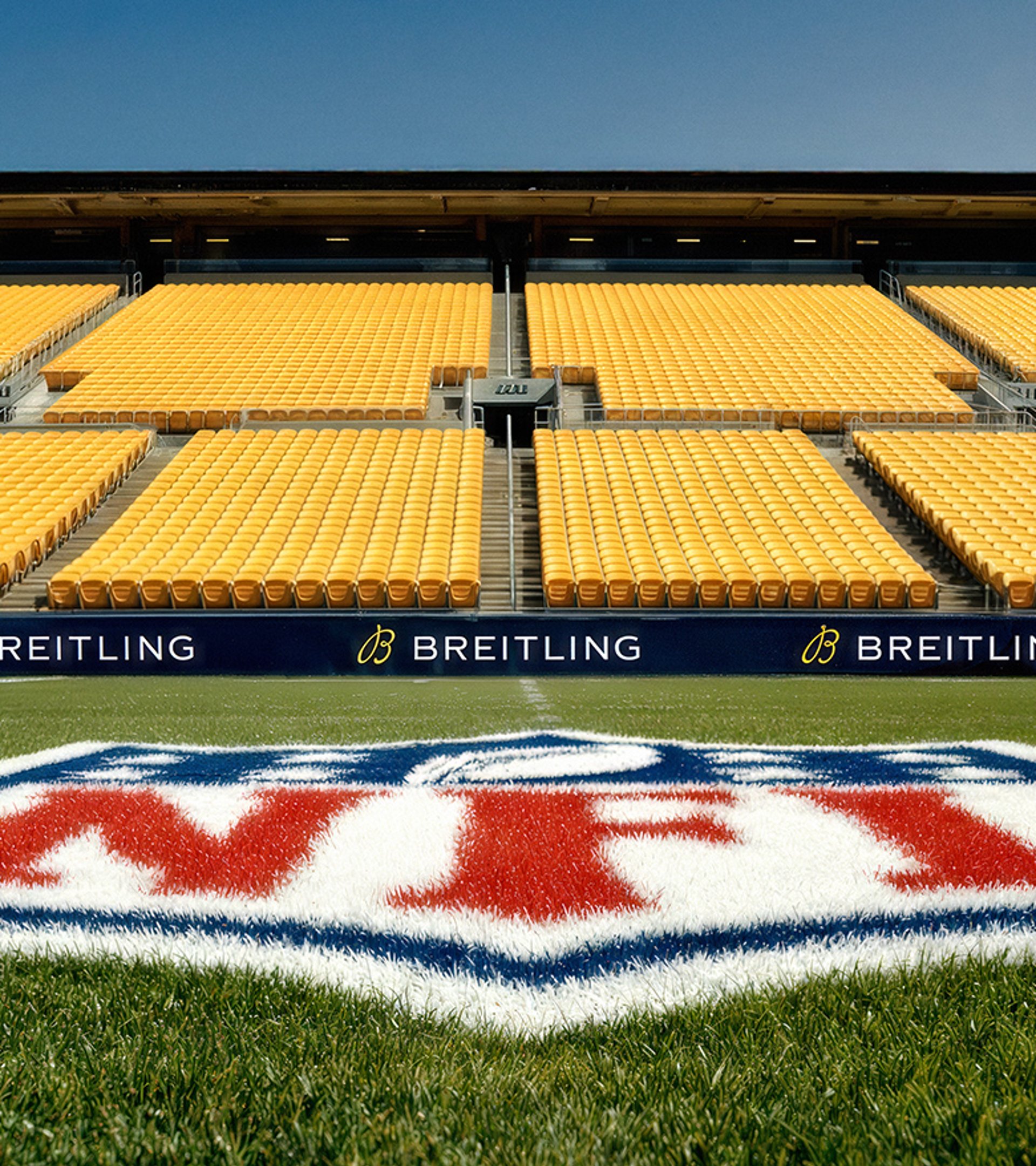 {generated} NFL field with bold midfield logo framed by empty yellow stands and prominent Breitling branding along the sidelines.