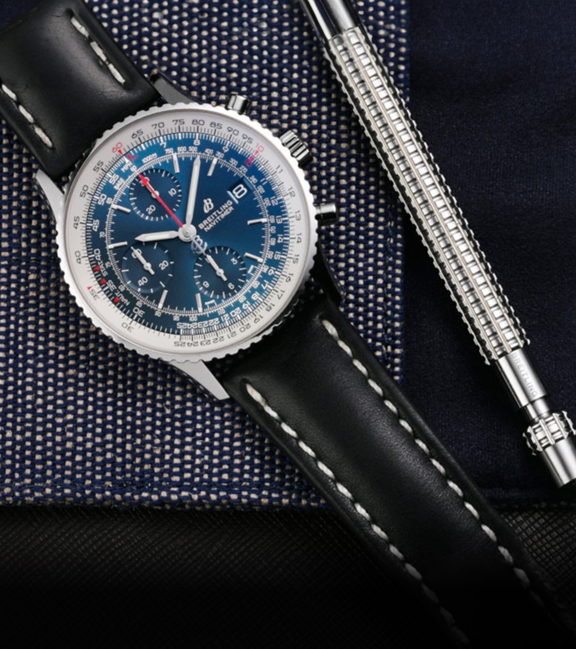 {generated} Breitling Navitimer with blue dial shown beside strap‑change tool and black leather Breitling strap on textured fabric