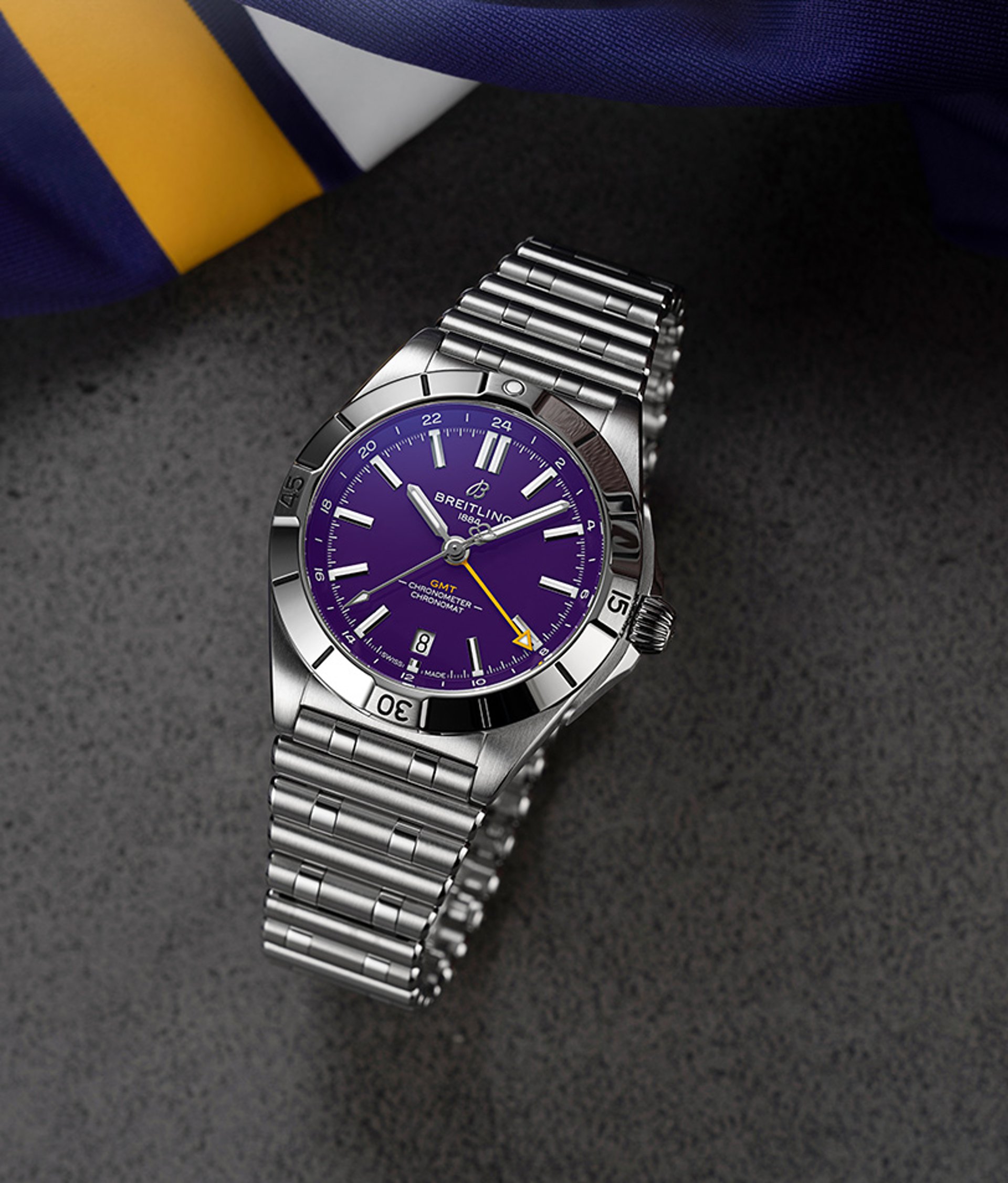 {generated} Breitling GMT watch with a purple dial and steel bracelet displayed on textured surface beside NFL-inspired team fabric.