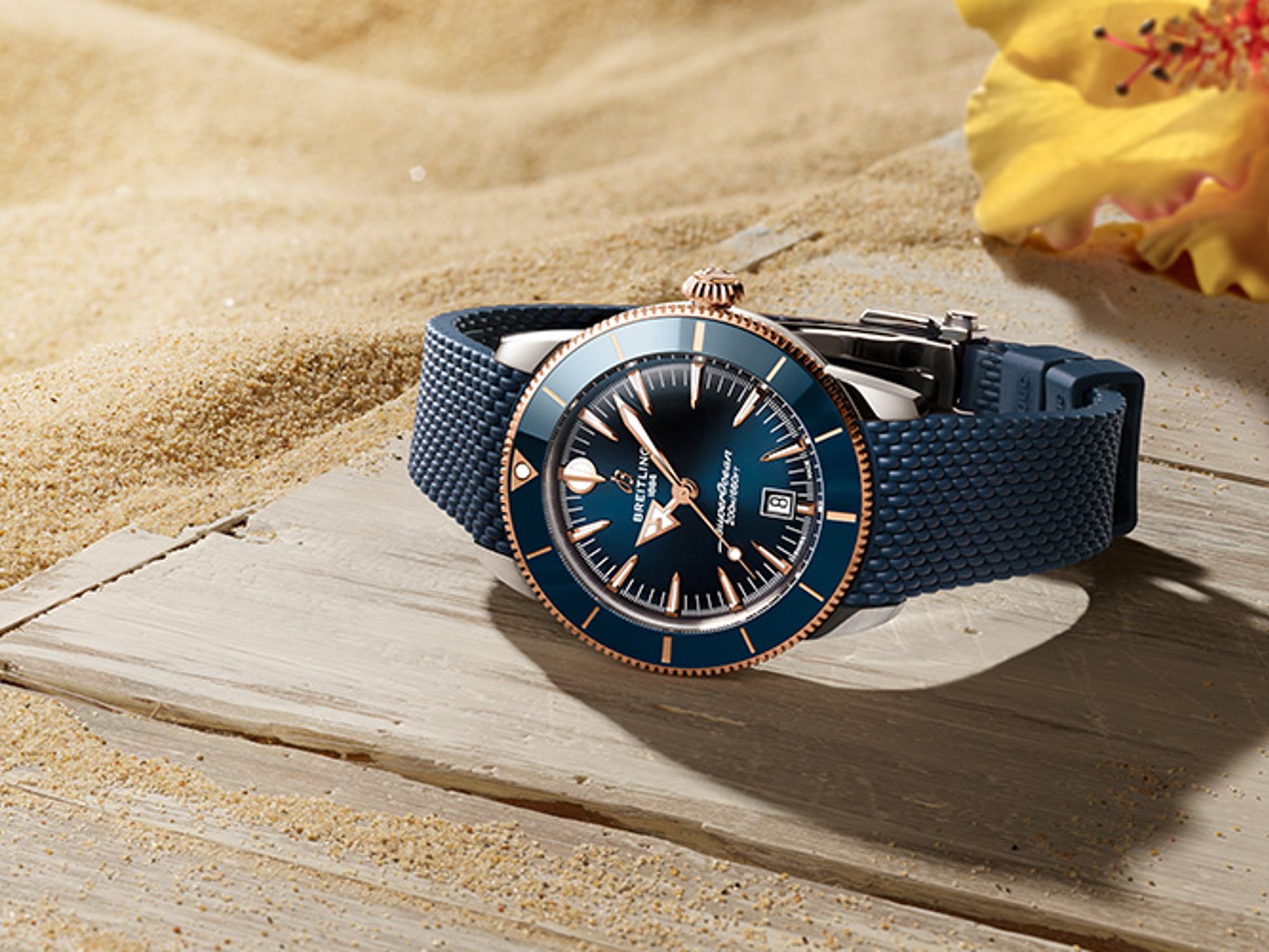 {generated} Breitling Superocean Heritage watch with blue dial and strap resting on sandy wood beside a bright yellow flower.