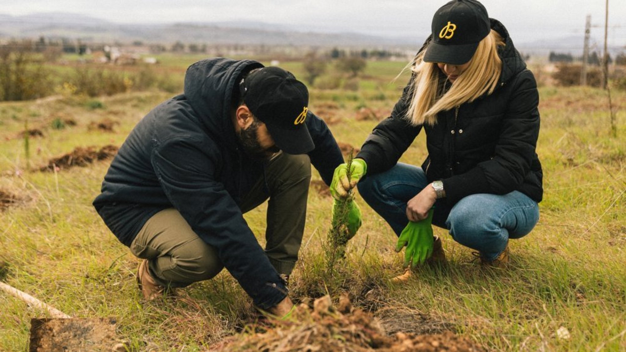 {generated} Two volunteers in Breitling caps plant a young tree in an open field, underscoring the brand’s commitment to sustainability.