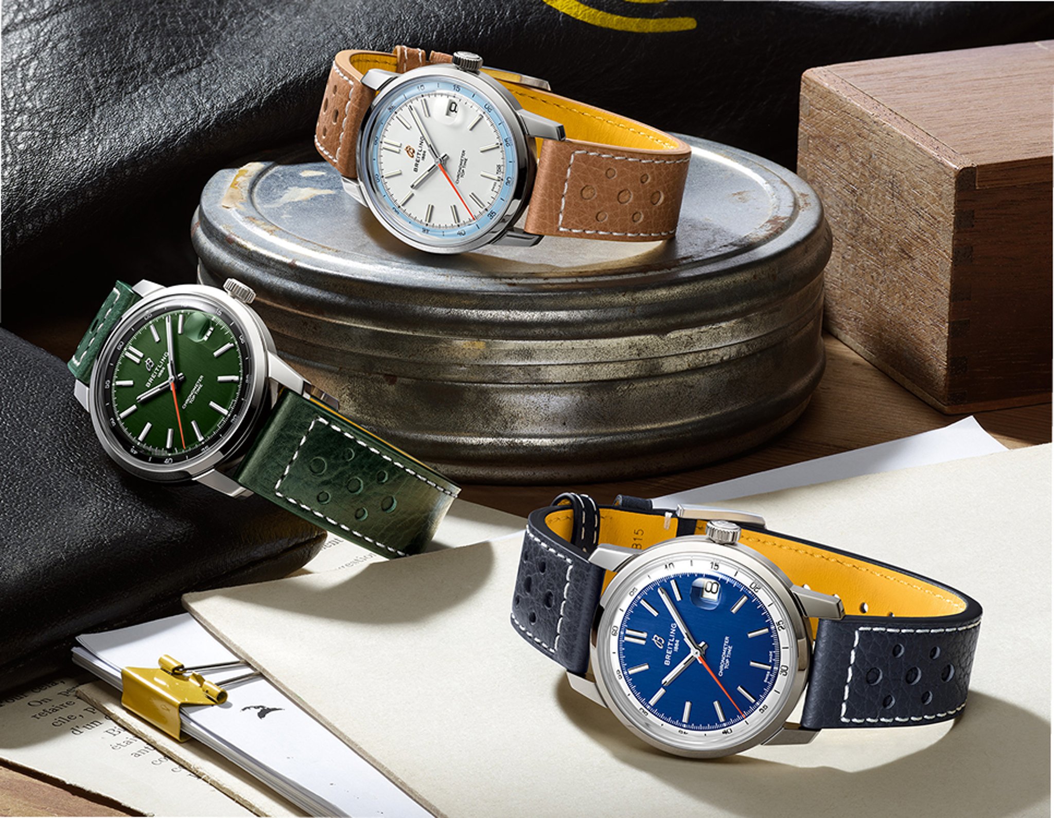 {generated} 三款Breitling Top Time以彩色錶盤與打孔錶帶陳列在具質感的平面上。