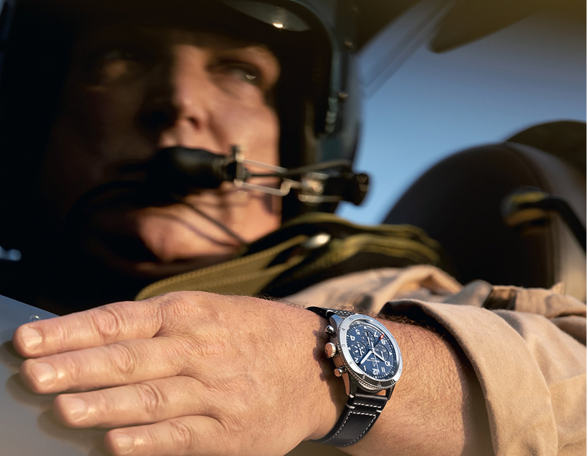 {generated} A pilot grips the cockpit frame while wearing a Breitling Classic Avi watch with a blue dial and stitched leather strap.