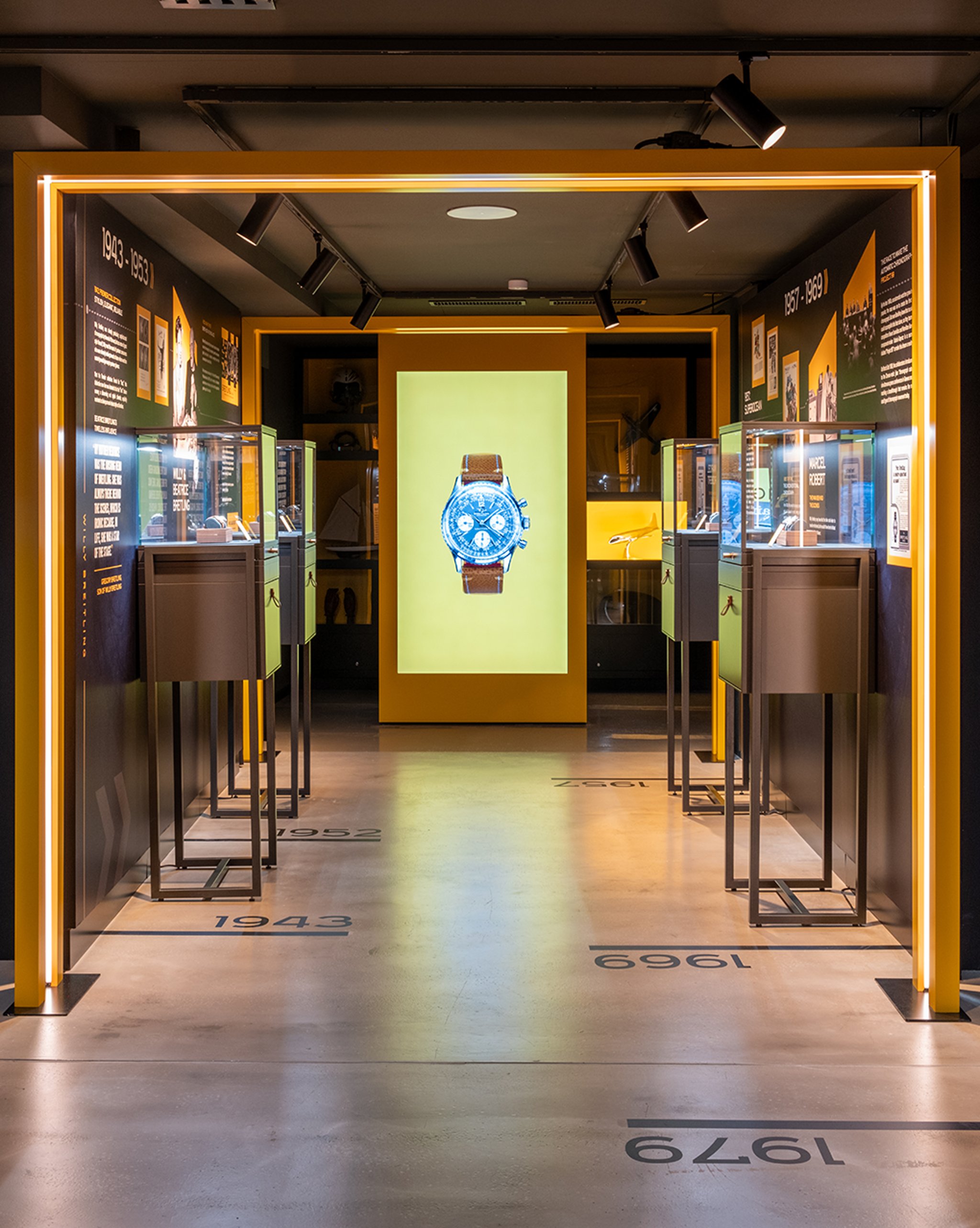 {generated} A museum-style gallery displays Breitling heritage with a central screen showcasing a Breitling watch on a yellow backdrop.
