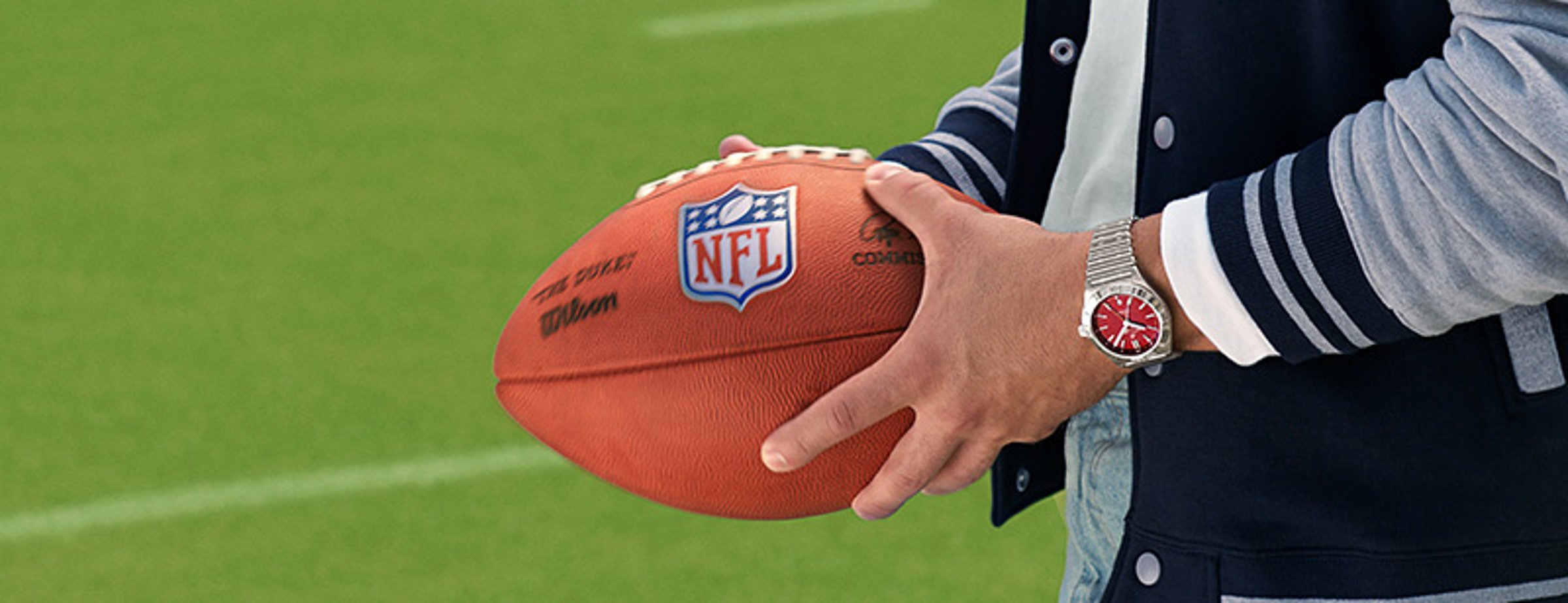 {generated} A person holding an NFL football on a bright pitch, wearing a red‑dial Breitling watch highlighted in a sporty setting.