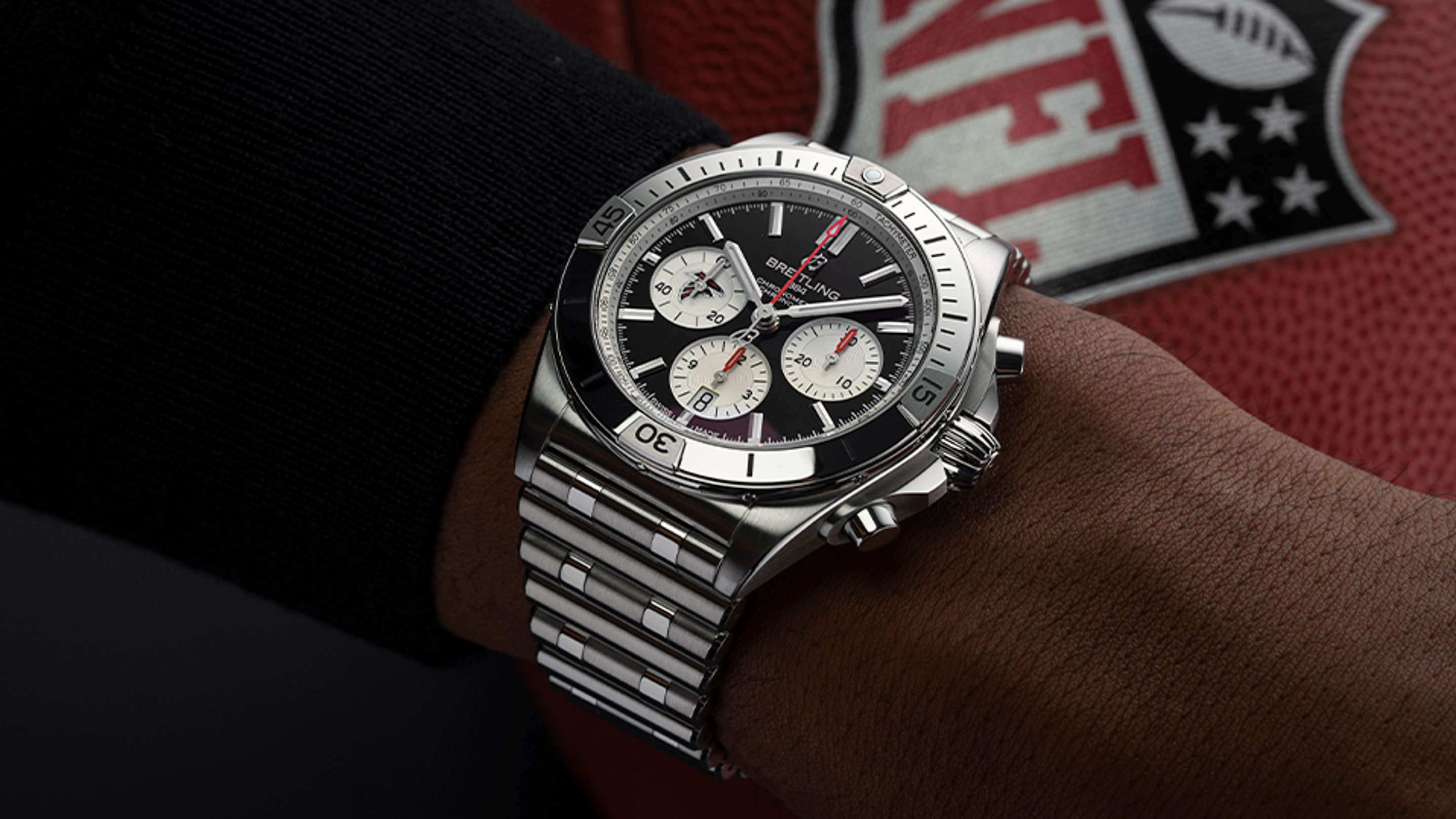 {generated} Breitling Chronomat on a wrist shown against an Atlanta Falcons NFL football, highlighting its polished steel design