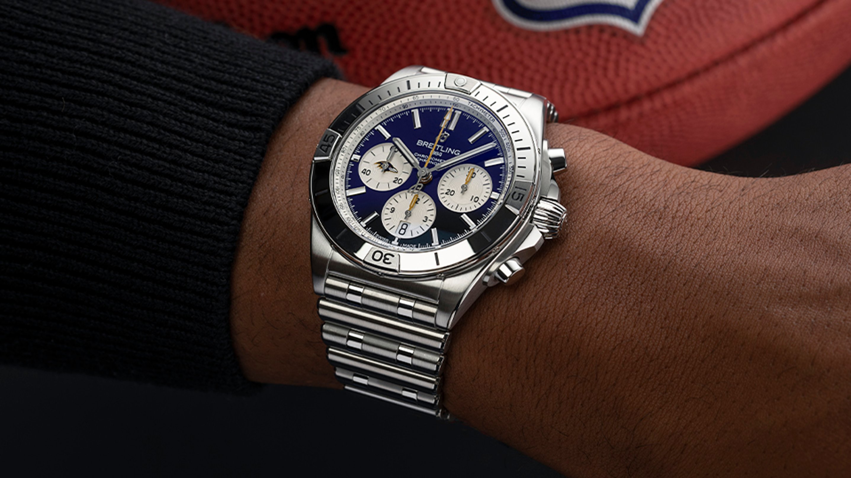 {generated} Breitling Chronomat with blue dial and Ravens detail on a wrist, shown against a football to highlight the NFL team theme