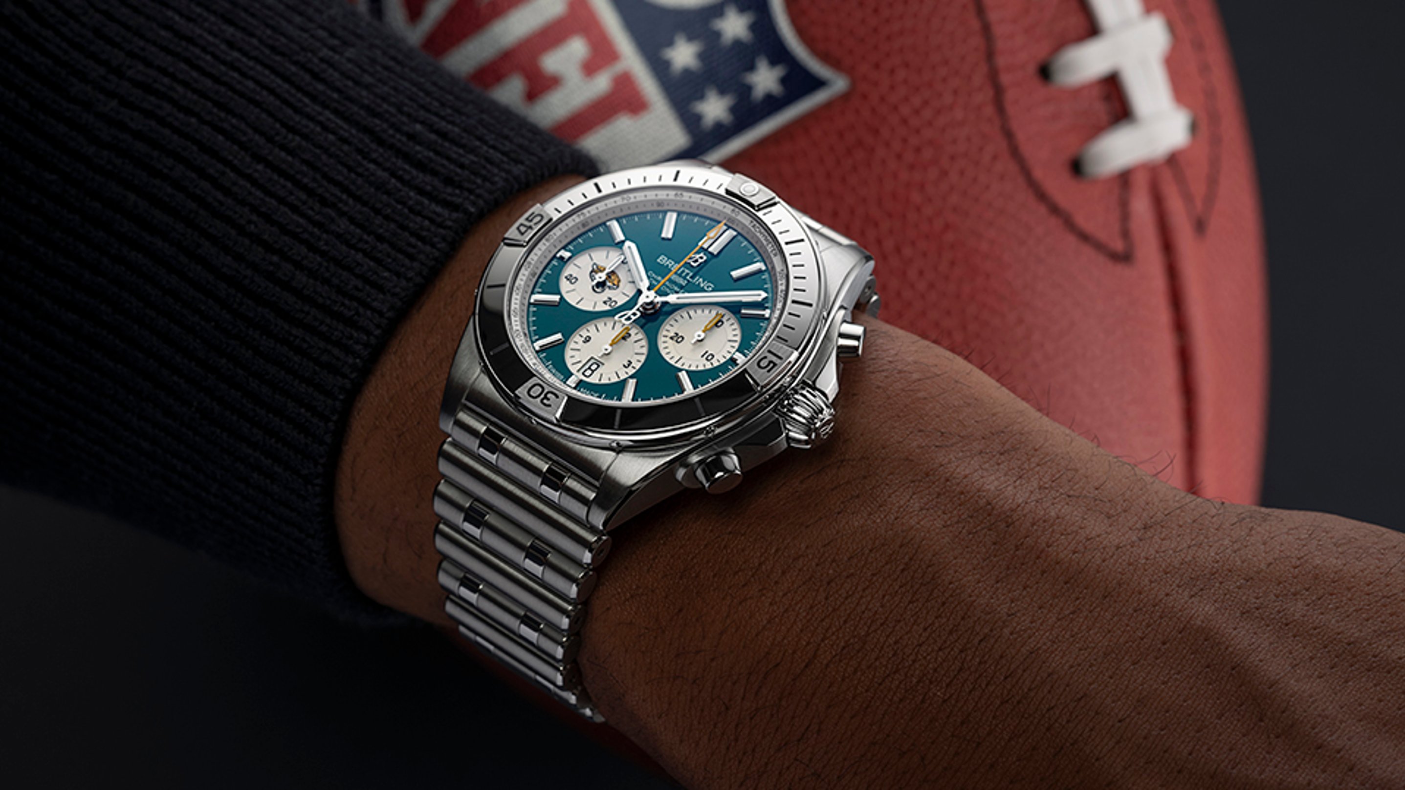 {generated} Breitling Chronomat shown on a wrist beside an NFL football, highlighting its teal dial and polished steel bracelet