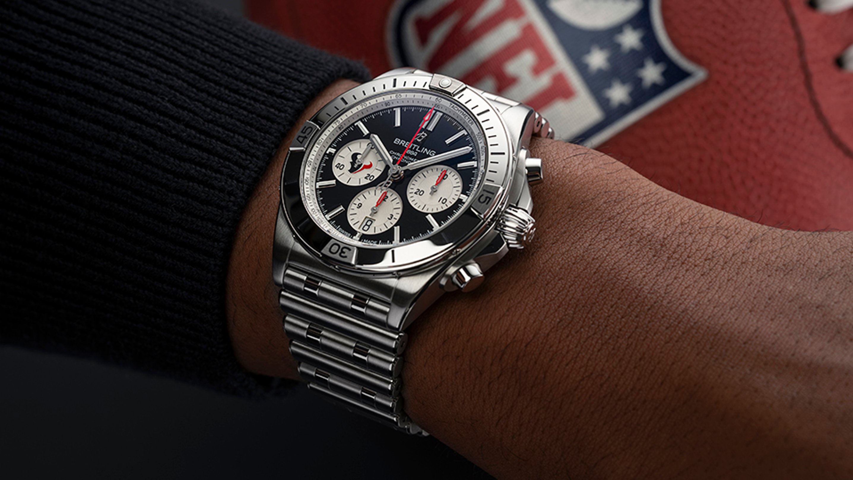 {generated} Breitling Chronomat on a wrist shown near a Houston Texans football, highlighting the sporty steel design and bold chronograph.