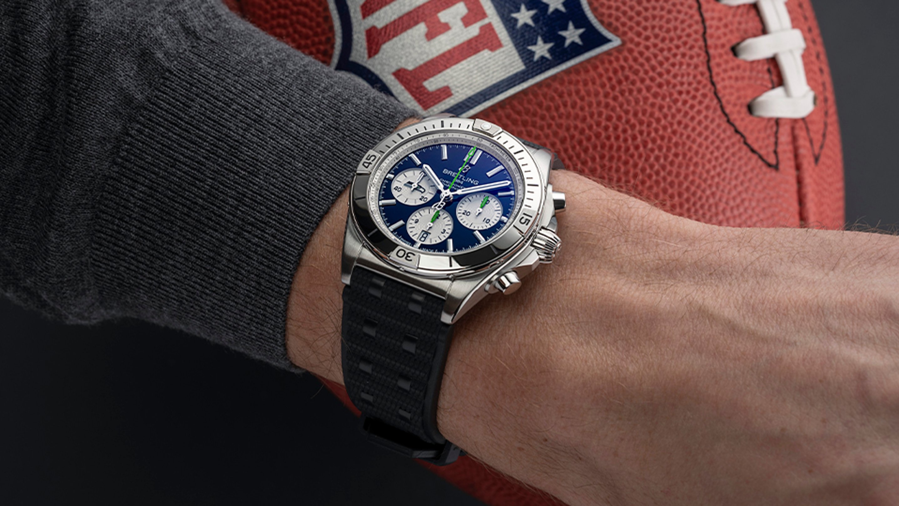 {generated} Breitling Chronomat with blue dial on a wrist beside a Seahawks-themed football, highlighting sporty precision style