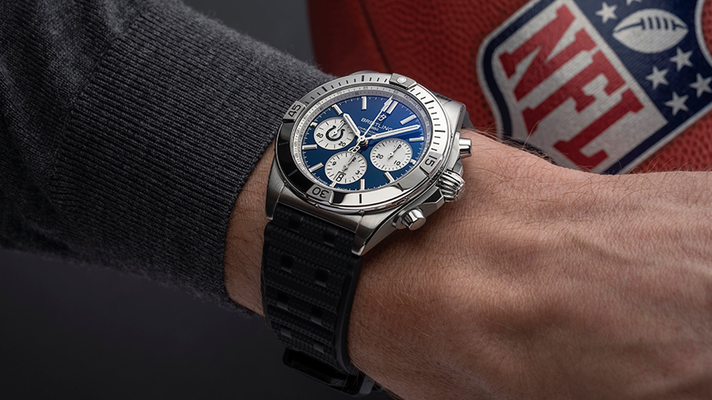 {generated} Breitling Chronomat with blue dial on a wrist beside an NFL football, highlighting sporty design and team spirit.