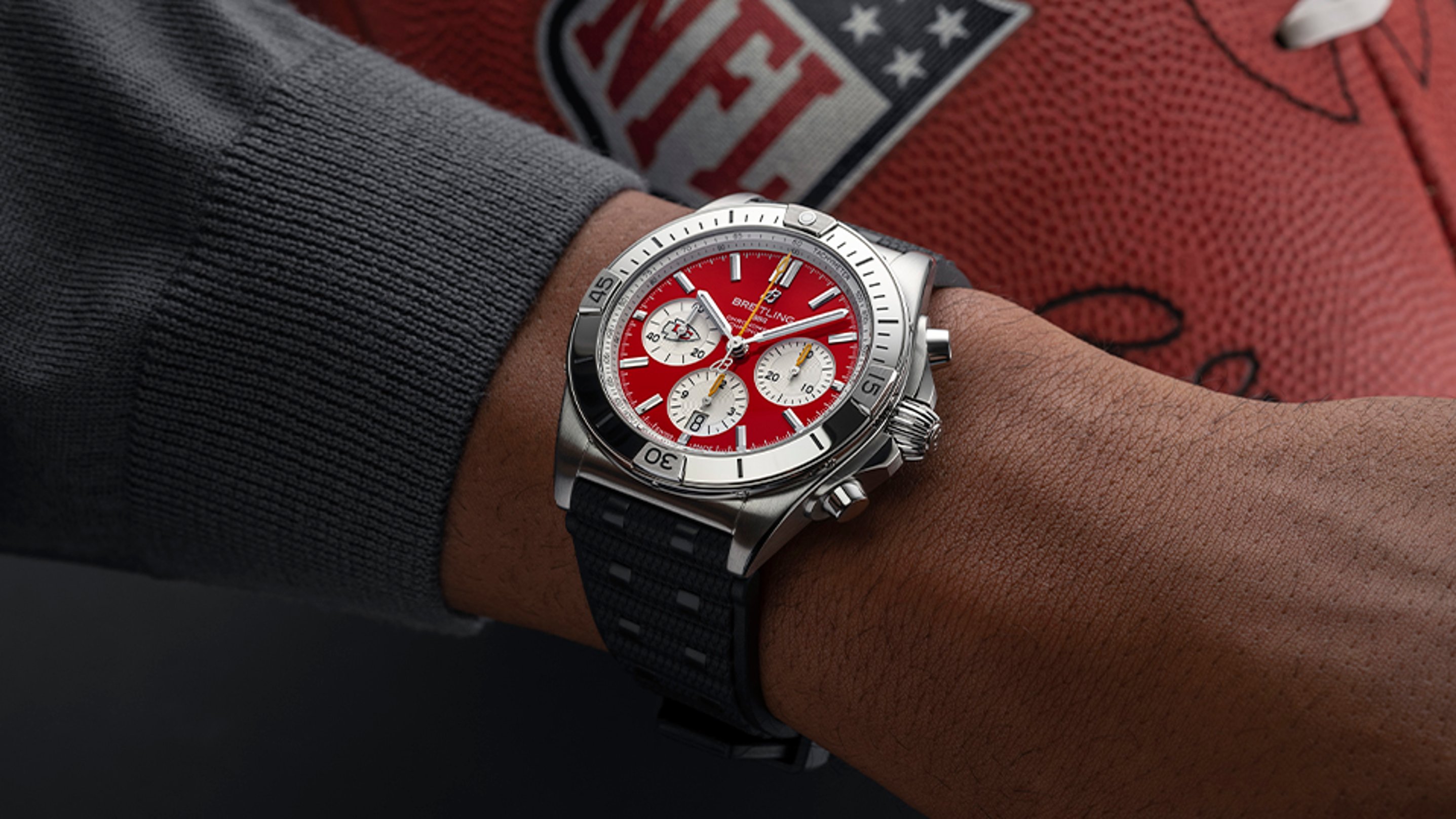 {generated} Breitling Chronomat Kansas City Chiefs edition on wrist, featuring red dial and steel case beside NFL football backdrop