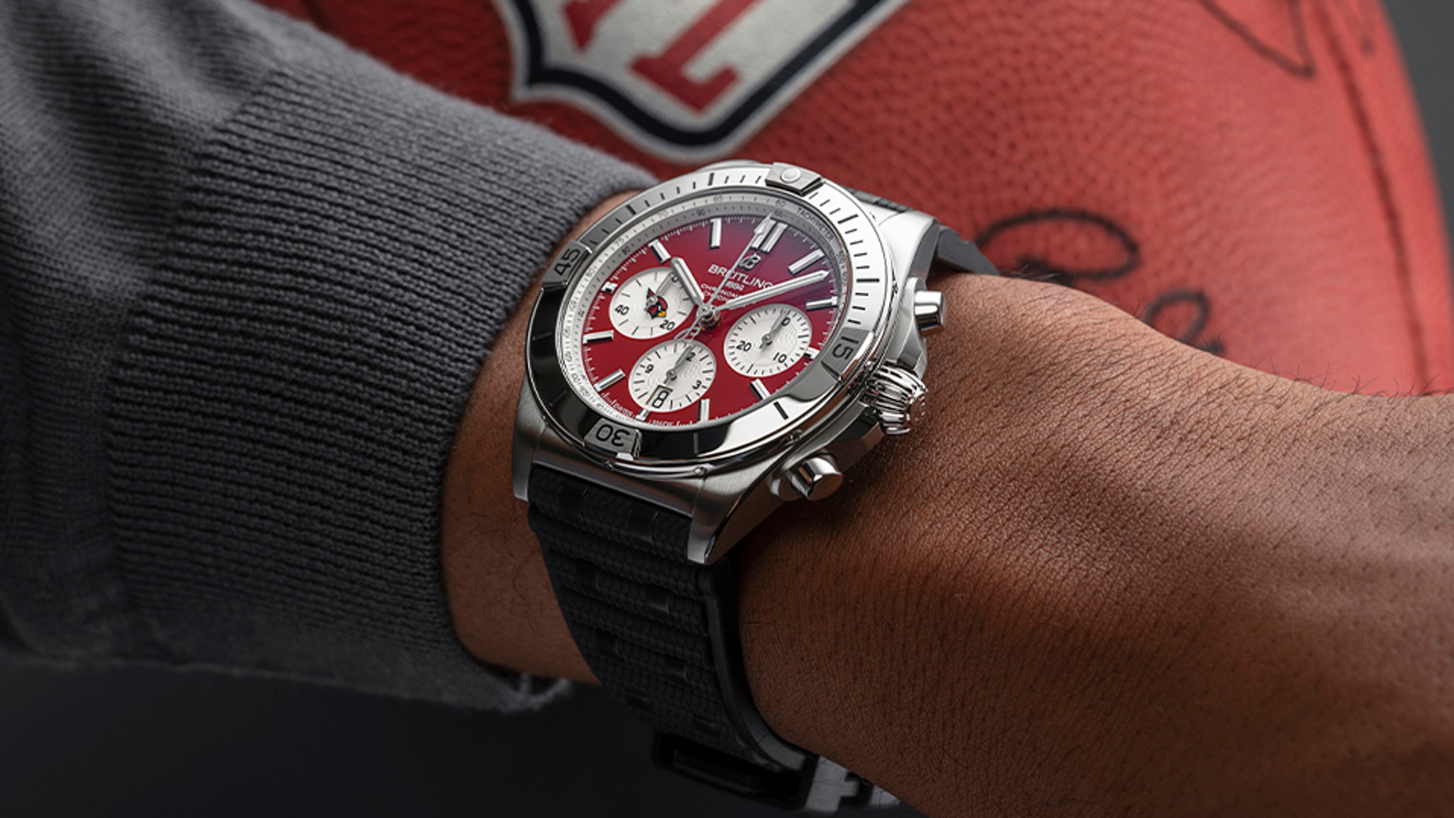 {generated} Breitling Chronomat with Arizona Cardinals red dial worn on a man’s wrist beside a textured football for team‑inspired style