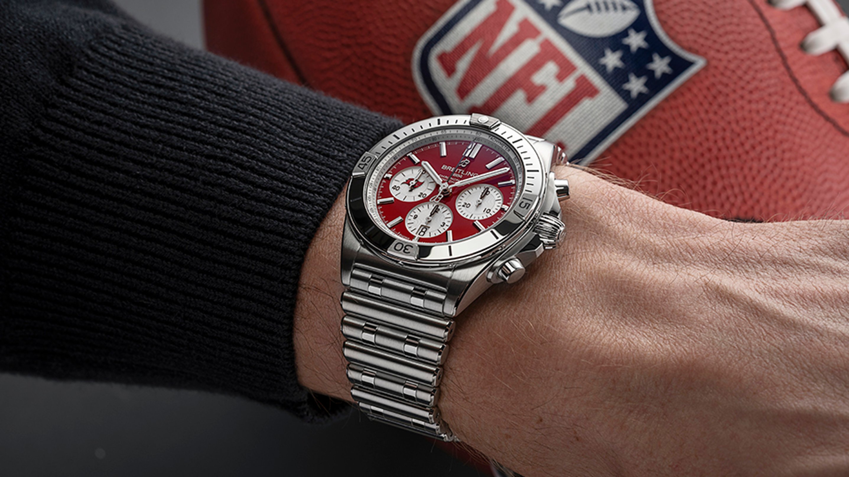 {generated} A wrist wearing a red-dial Breitling Chronomat beside an NFL football highlights the Tampa Bay Buccaneers themed design