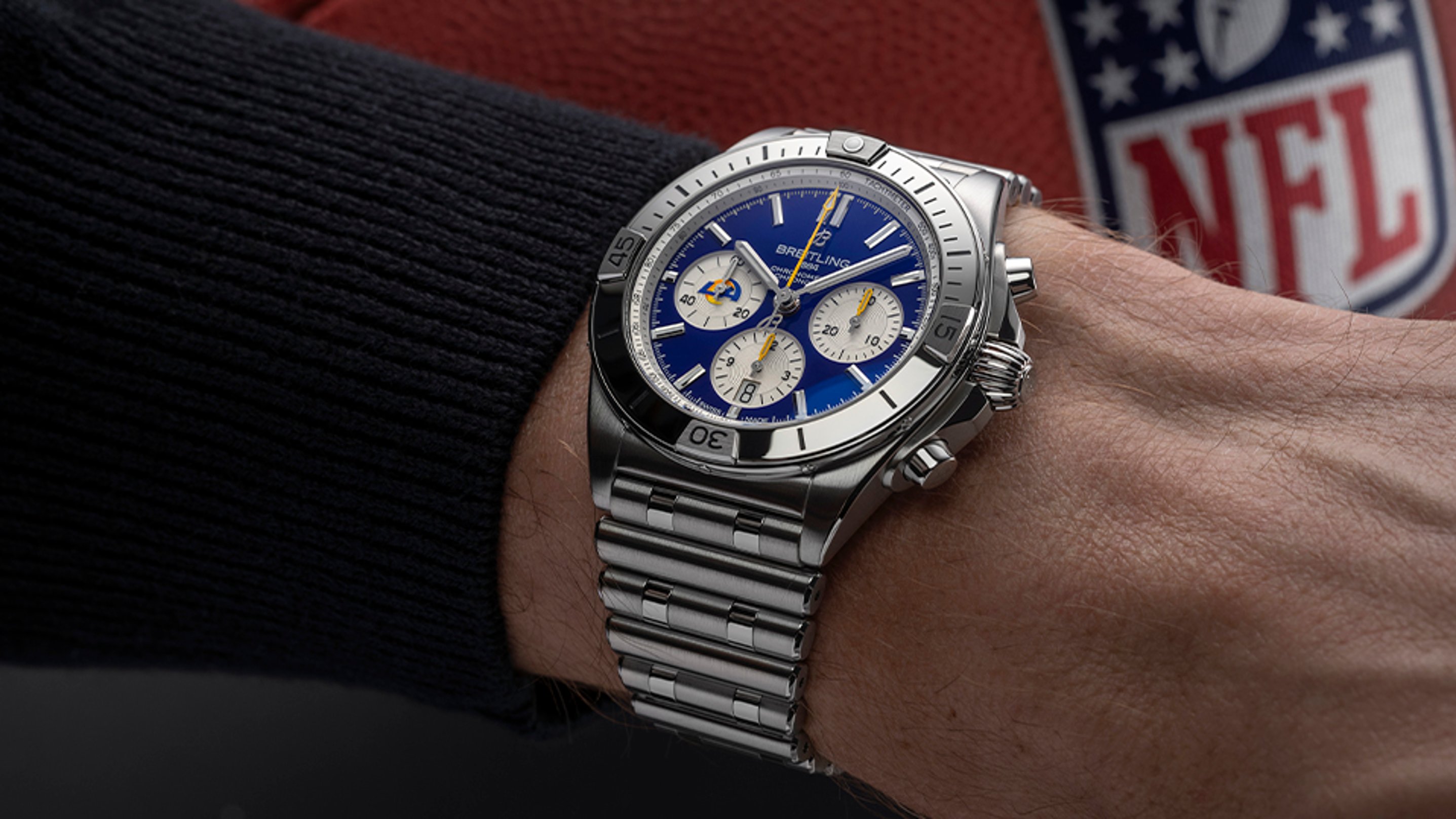 {generated} Reloj Breitling con esfera azul y detalles de Los Angeles Rams en una muñeca junto a un balón de la NFL