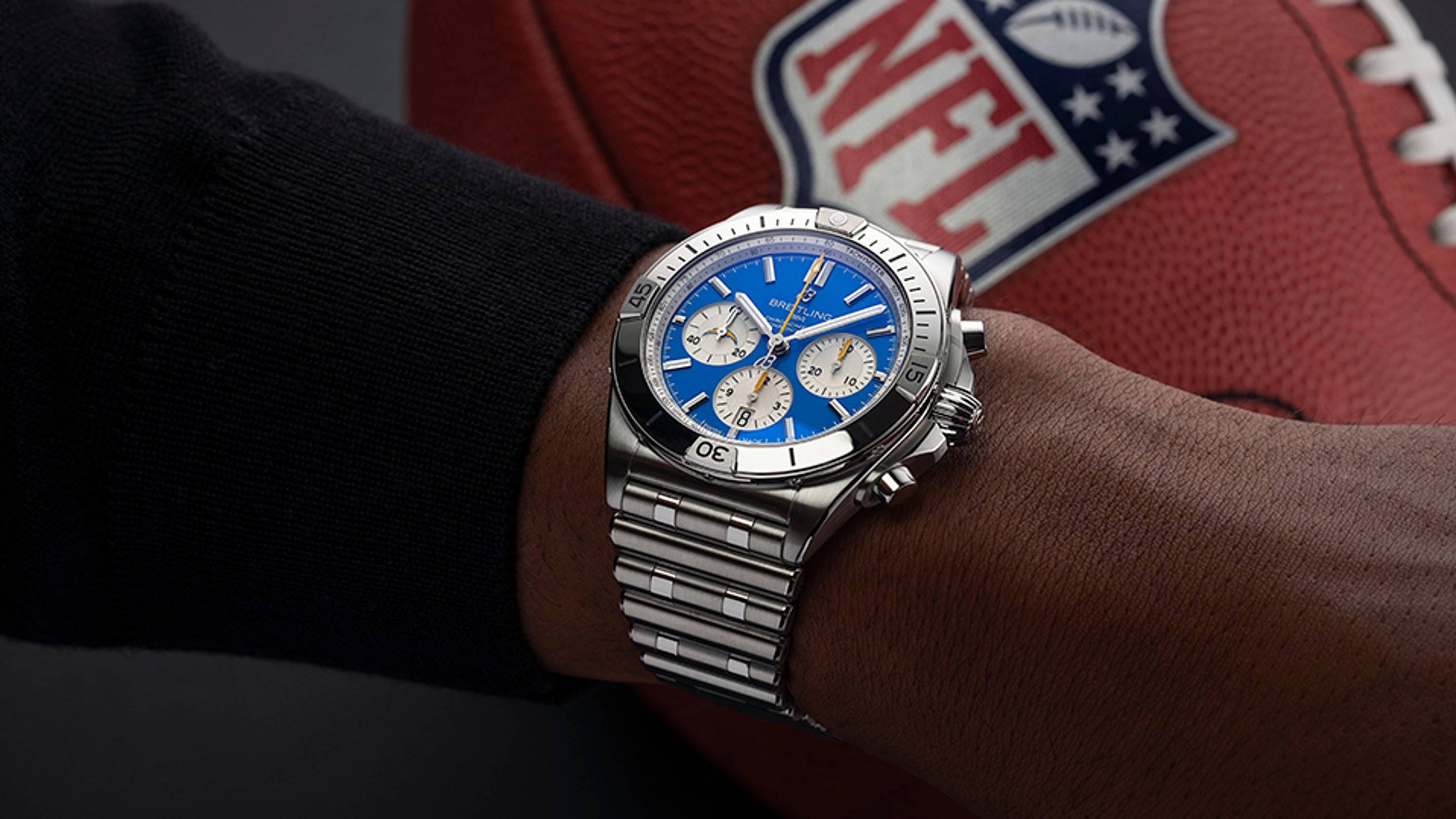 {generated} Breitling Chronomat with blue dial on a wrist beside an NFL football, highlighting the Los Angeles Chargers theme.