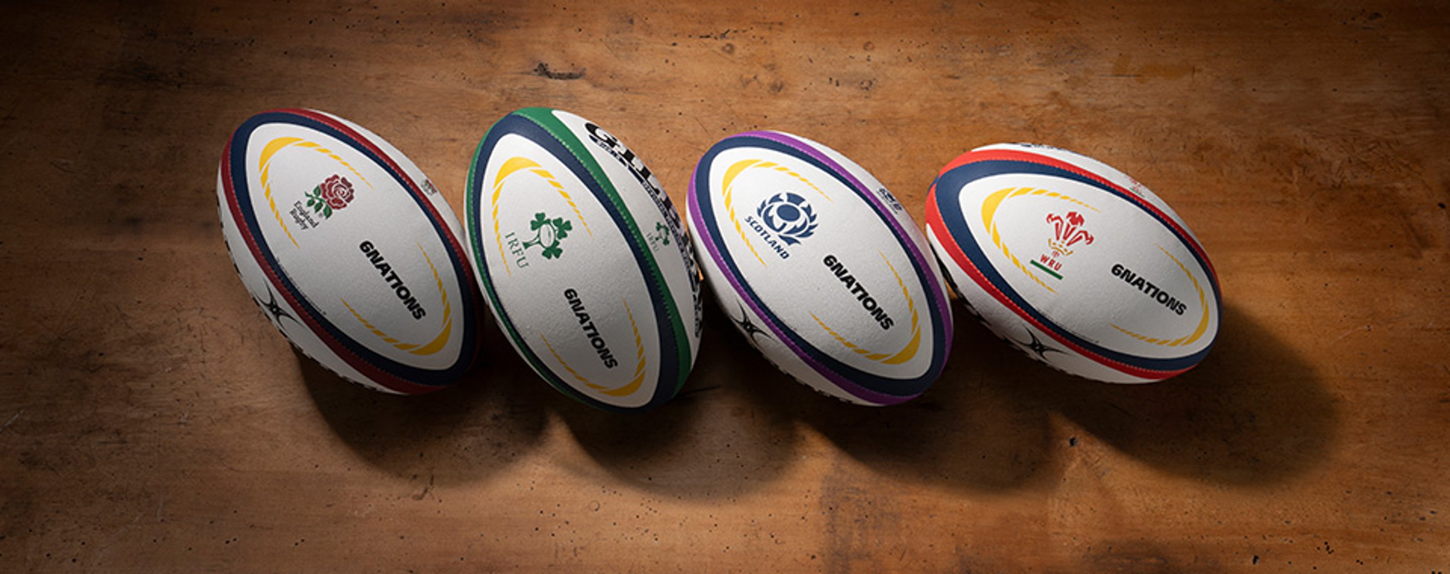 {generated} Four branded rugby balls from England, Ireland, Scotland and Wales arranged on a wooden surface for Six Nations 2025