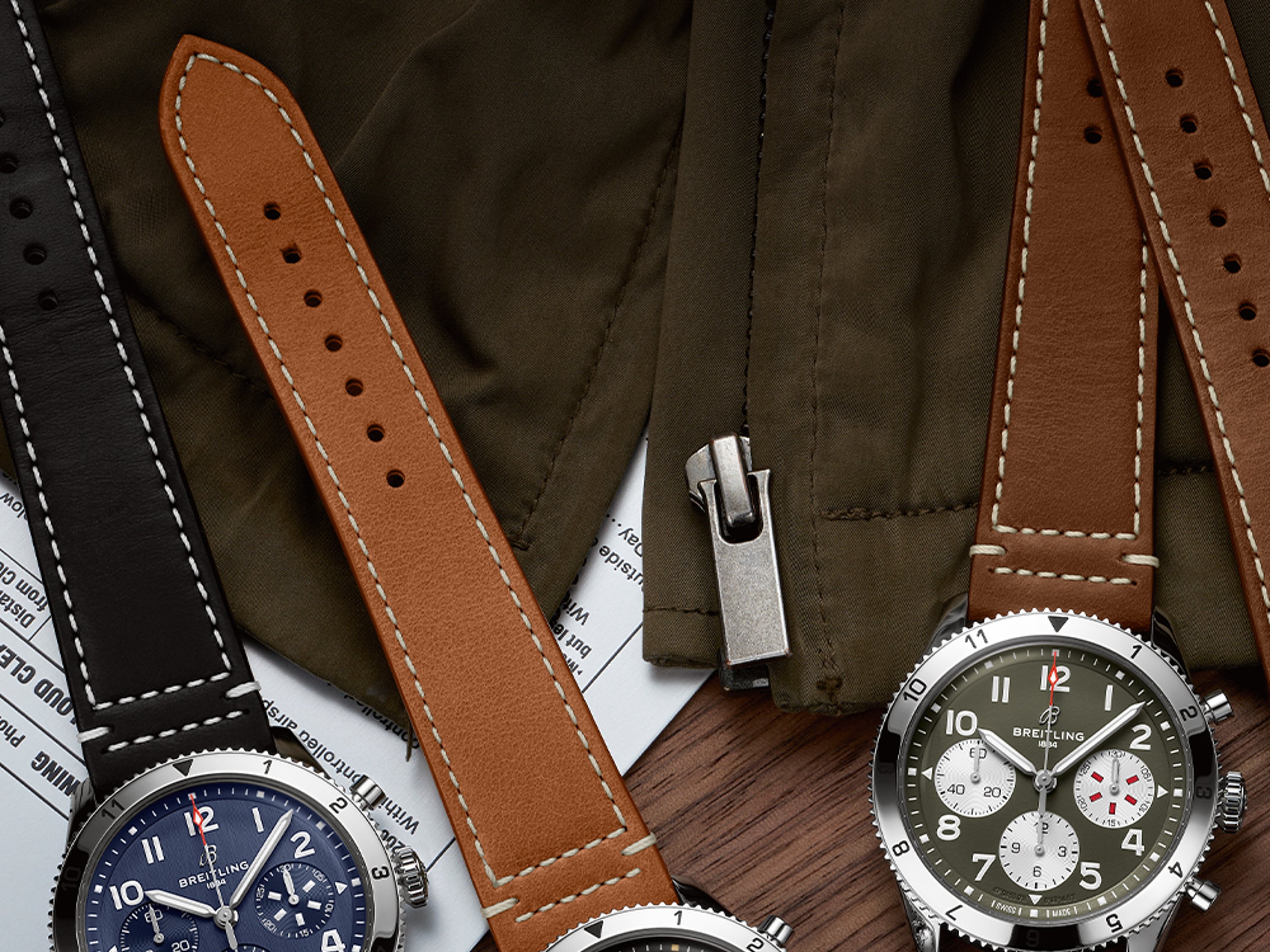 Three Classic AVI with different colored, dark leather straps on a dark brown table.