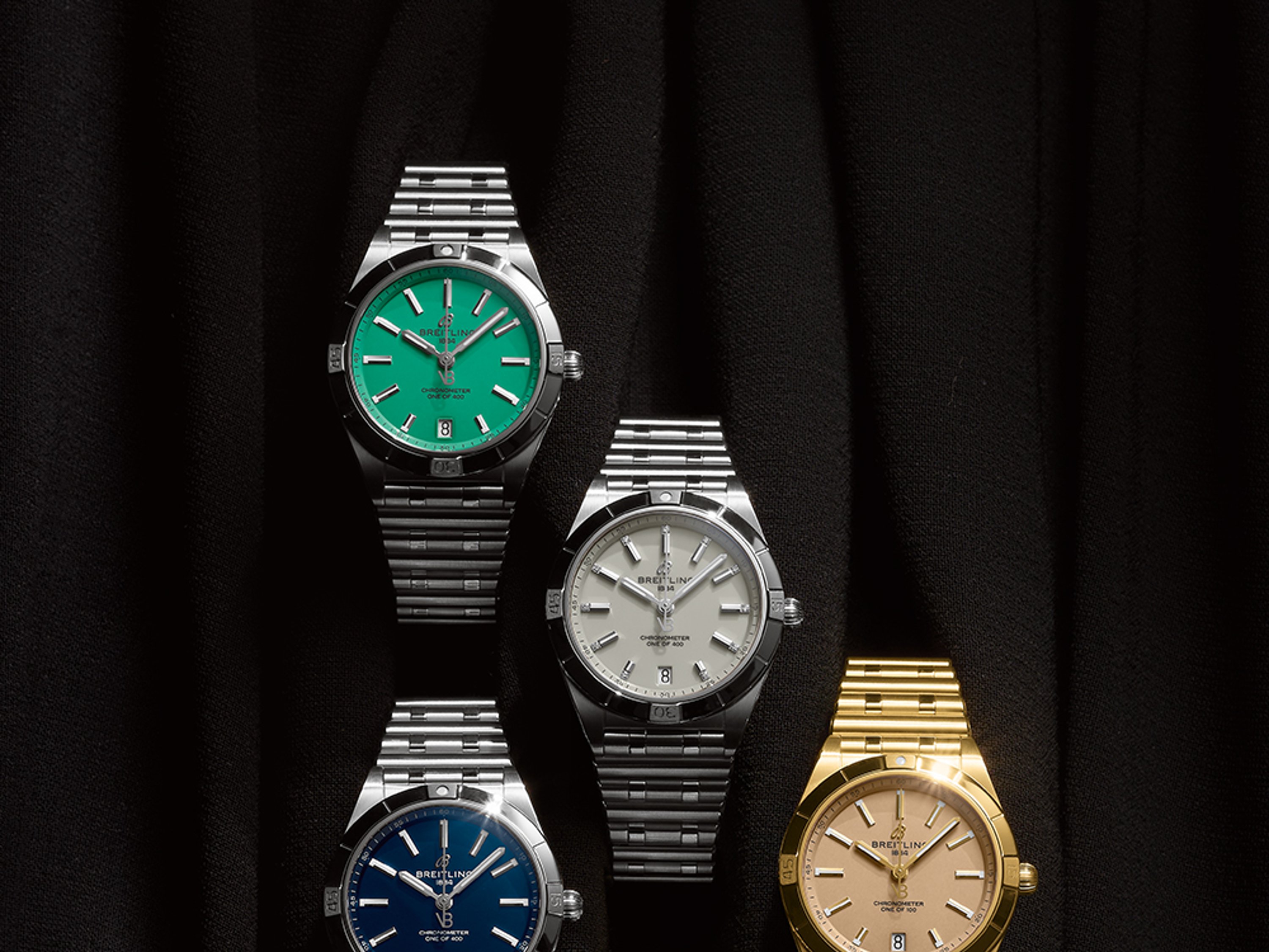 Three silver and three gold Chronomat watches with different-colored dials against a black background.