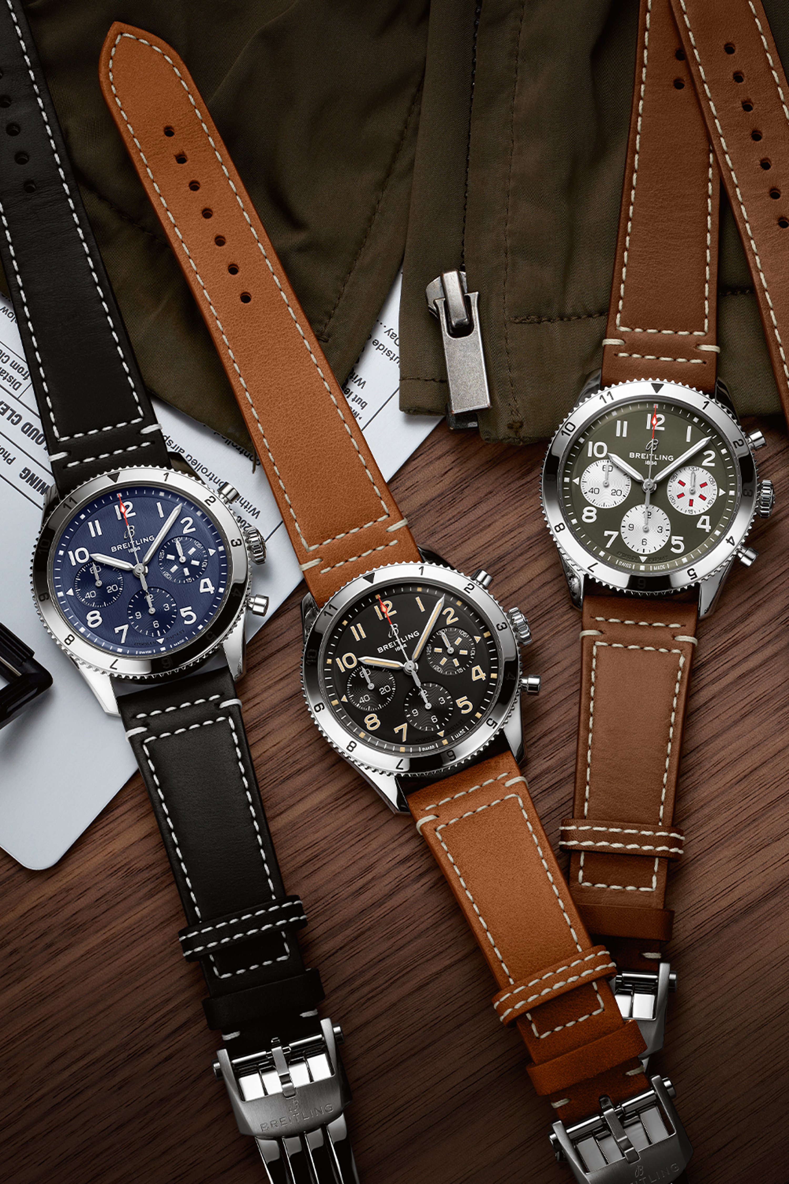 Three Classic AVI with different colored, dark leather straps on a dark brown table.