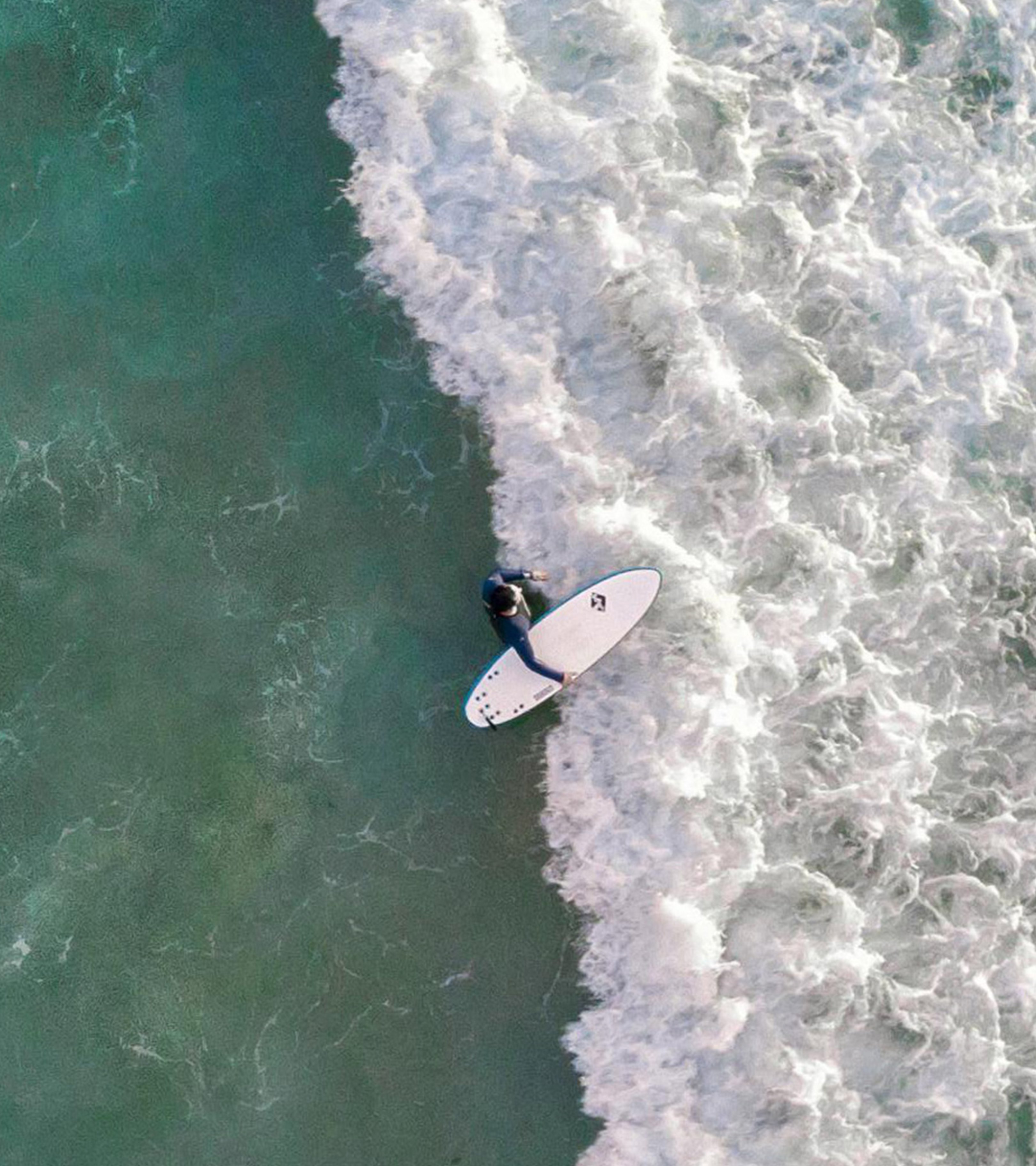 {generated} Un surfeur progresse sur des vagues écumeuses dans une mer émeraude, reflétant l’engagement de Breitling pour la durabilité marine.