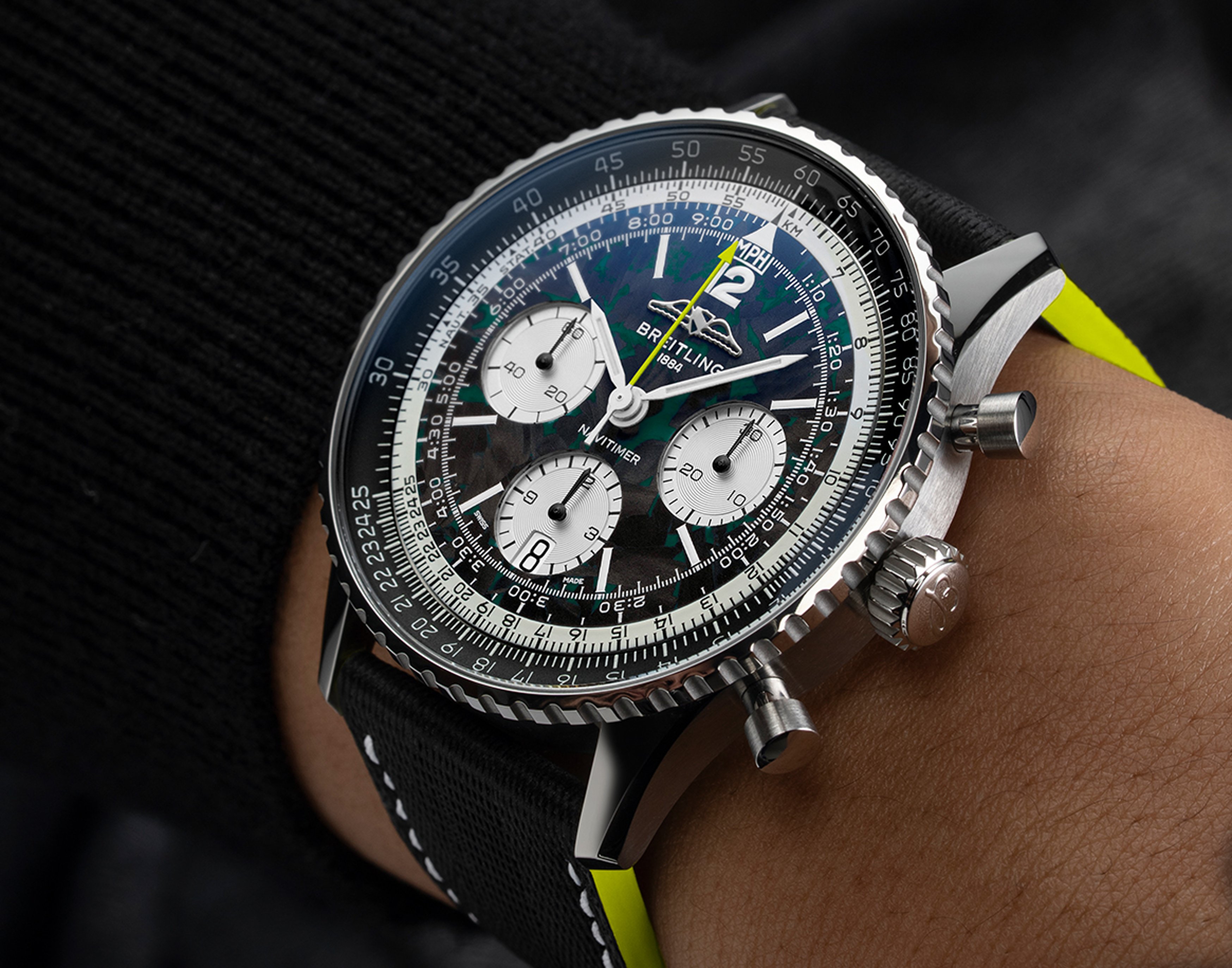 {generated} Breitling Navitimer shown in close-up with black dial and fabric strap, set against a yellow backdrop for partnership.