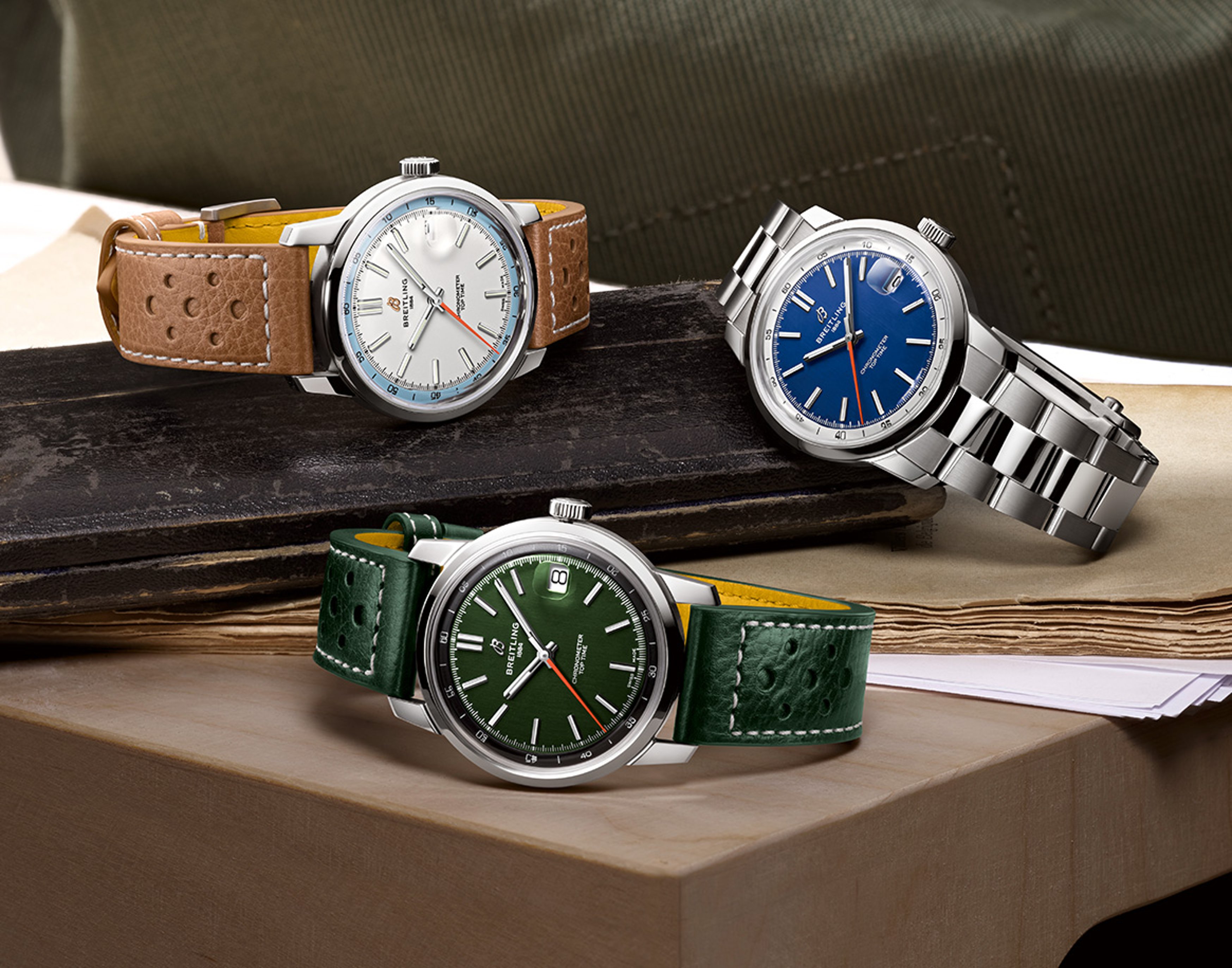 {generated} 銀色・青・緑の文字盤を備えた3本のBreitling Top Timeが古い本の上に並ぶ落ち着いたスタジオ構成