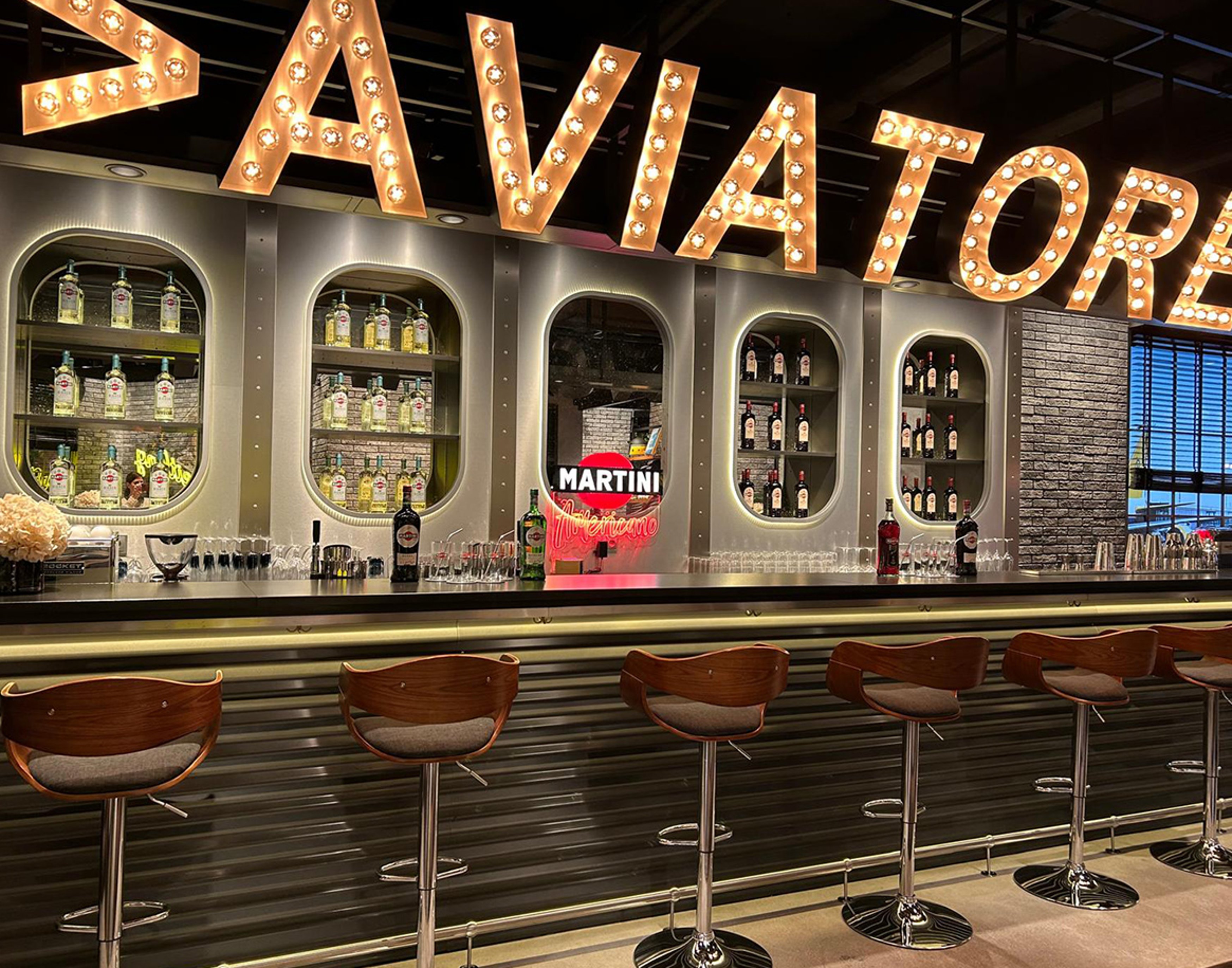 {generated} Vivace Martini bar con insegne luminose e sgabelli moderni che richiamano lo spirito dinamico della Breitling Top Time.