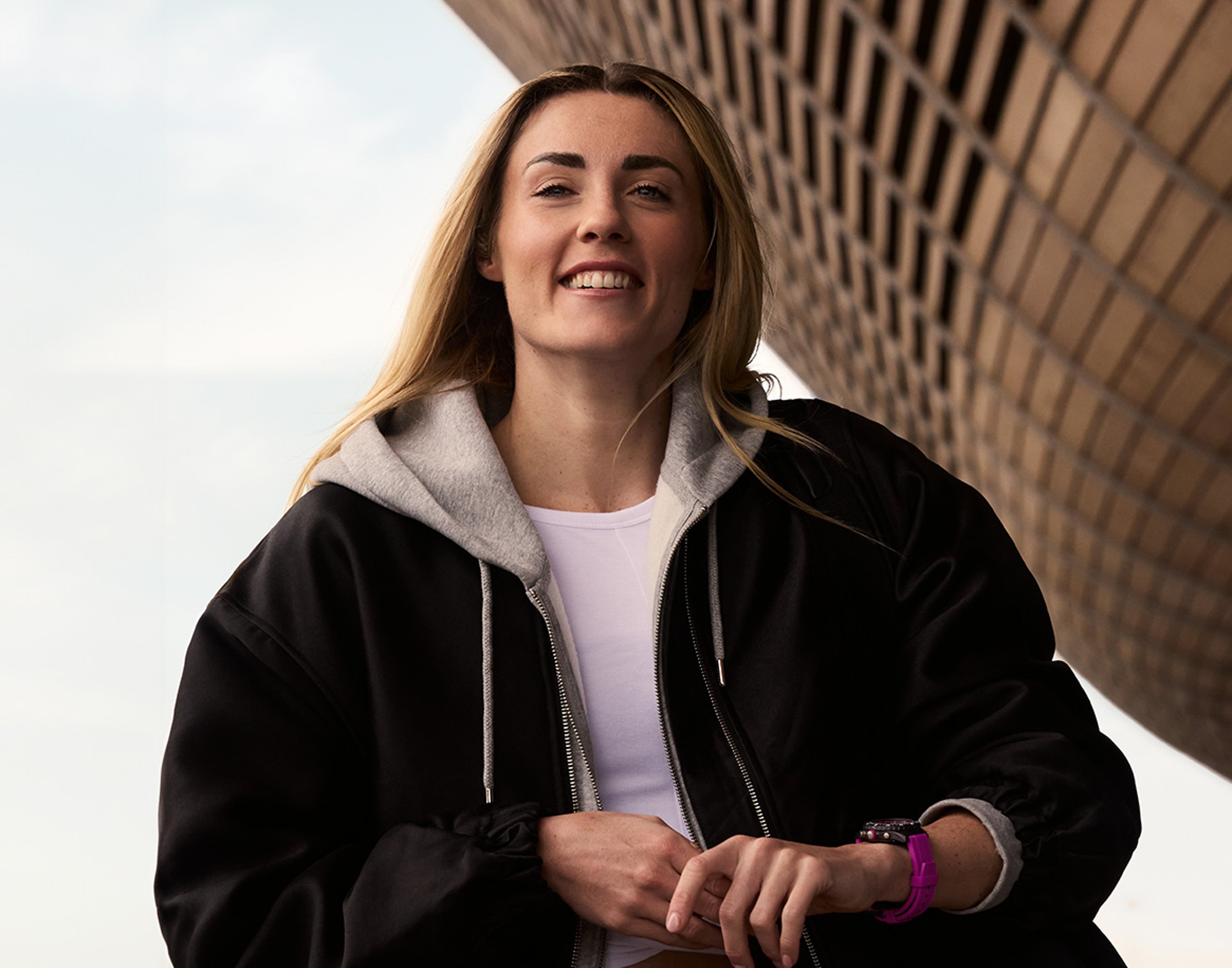 {generated} A female Breitling ambassador in casual layers beneath an architectural structure, highlighting athletic poise.