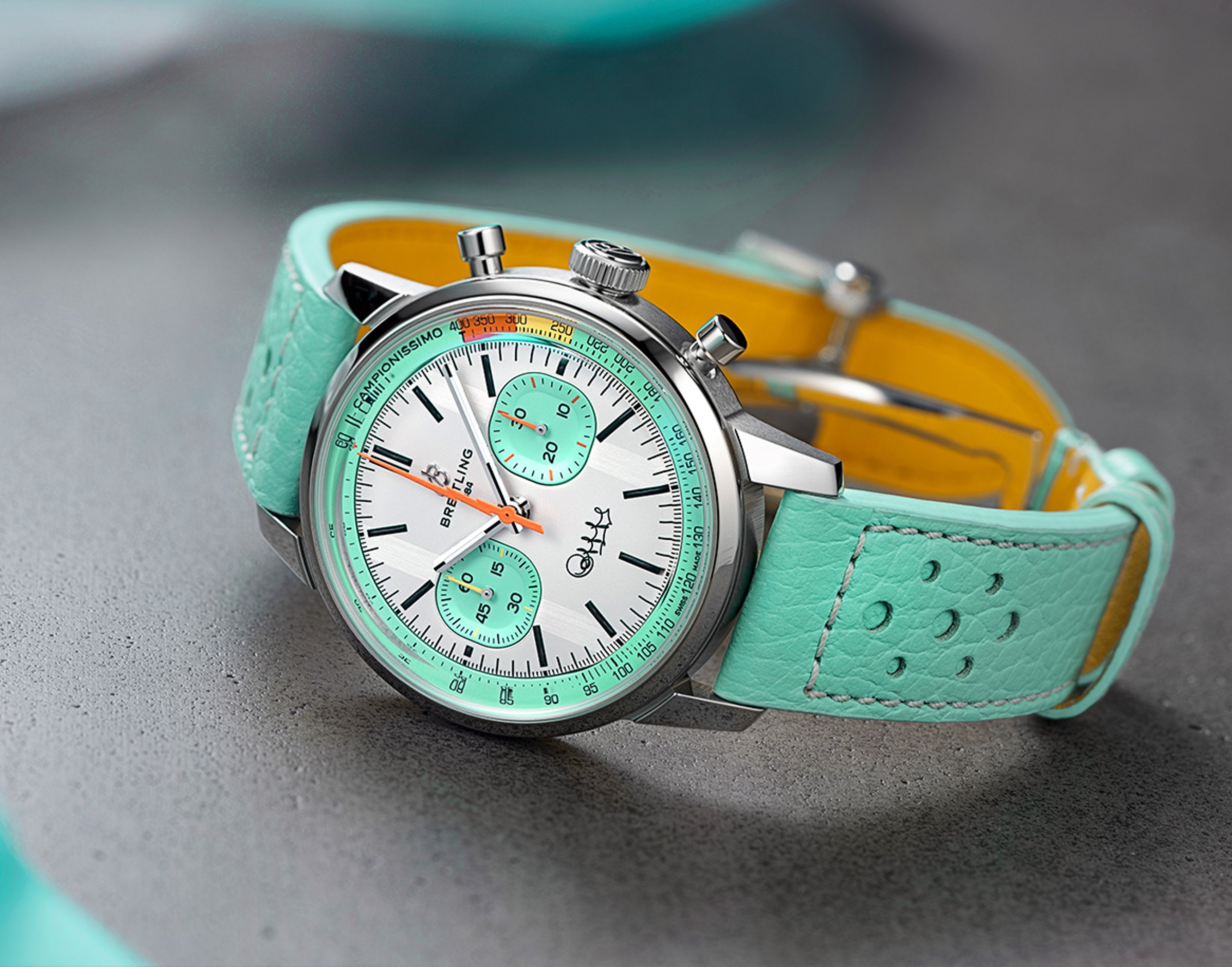 {generated} Breitling Bartali watch with a mint leather strap and white dial with turquoise subdials presented on a grey surface