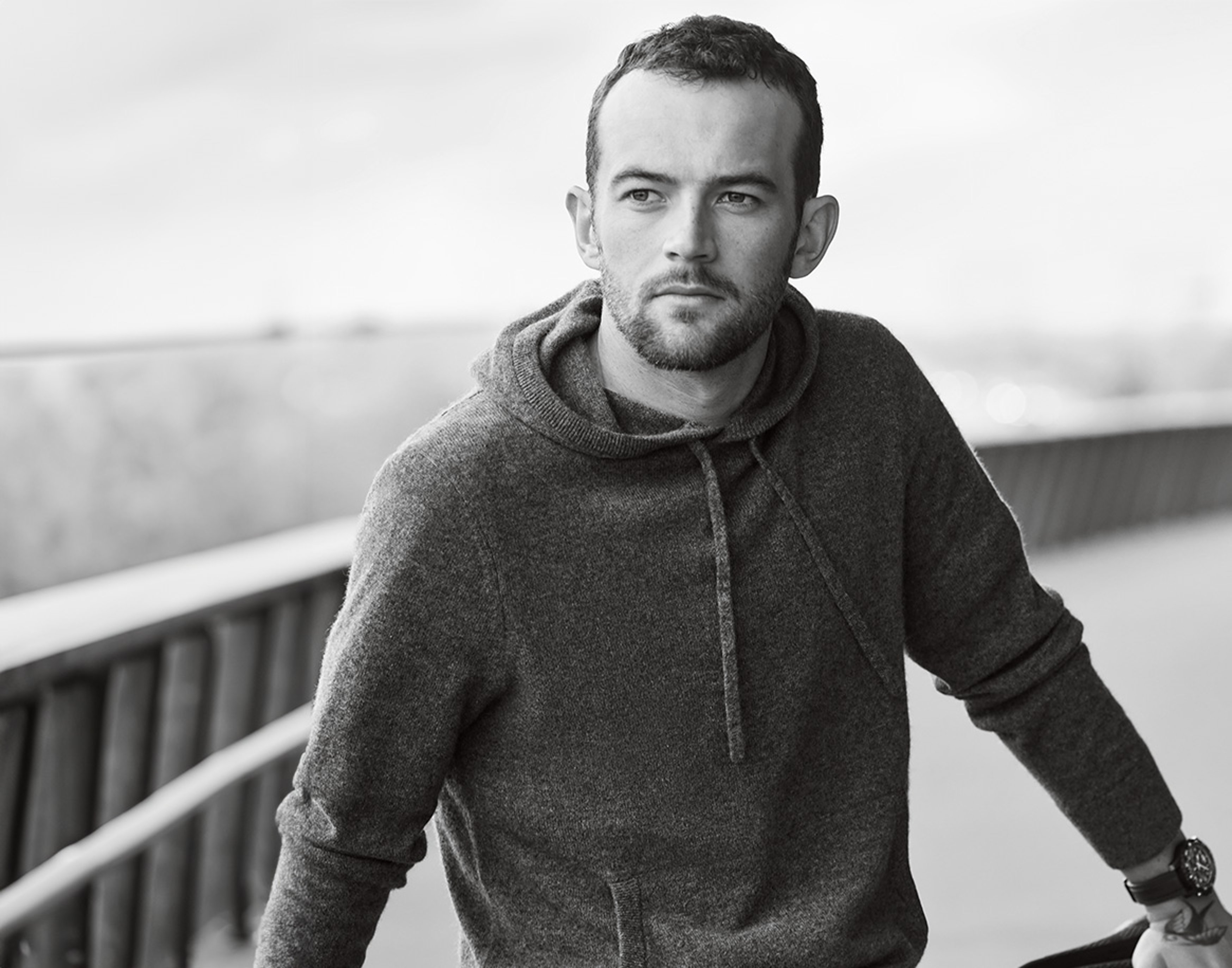 {generated} A man rests by a railing outdoors, highlighting a Breitling watch on his wrist in a calm and understated monochrome scene