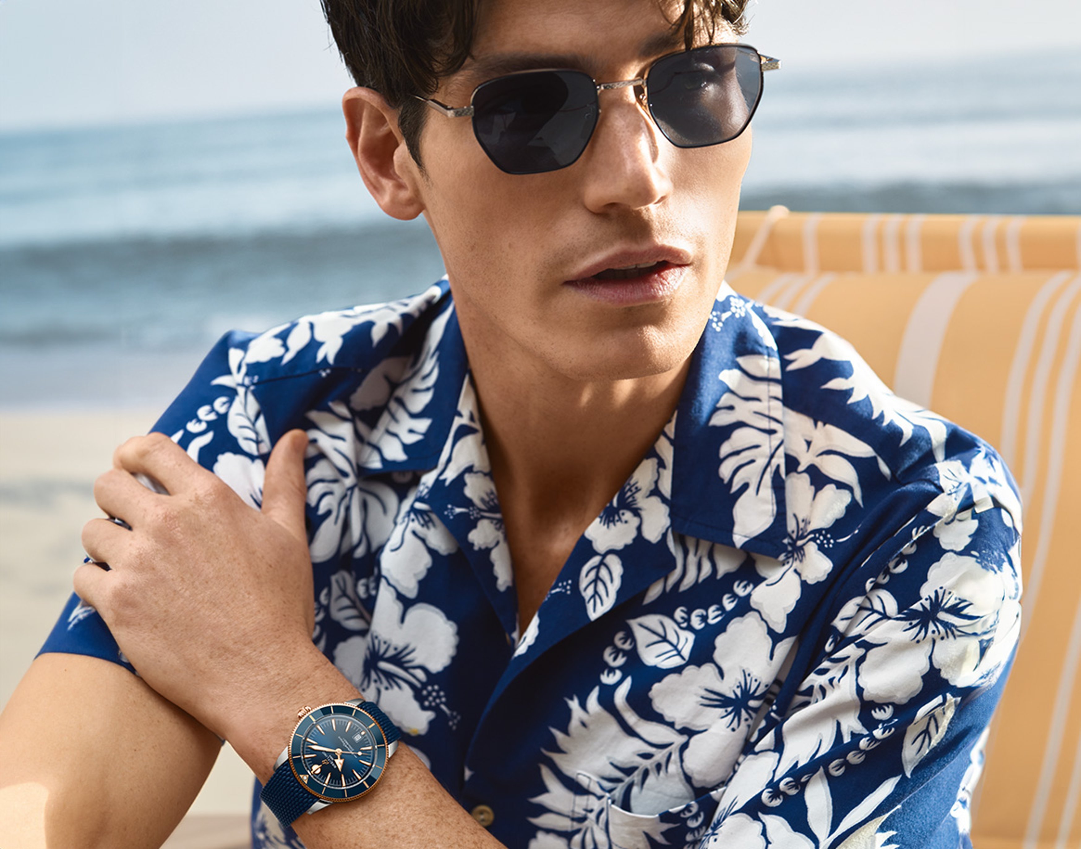 {generated} Man on a beach wearing sunglasses and a Breitling Superocean Heritage watch with blue dial and strap in a summer scene