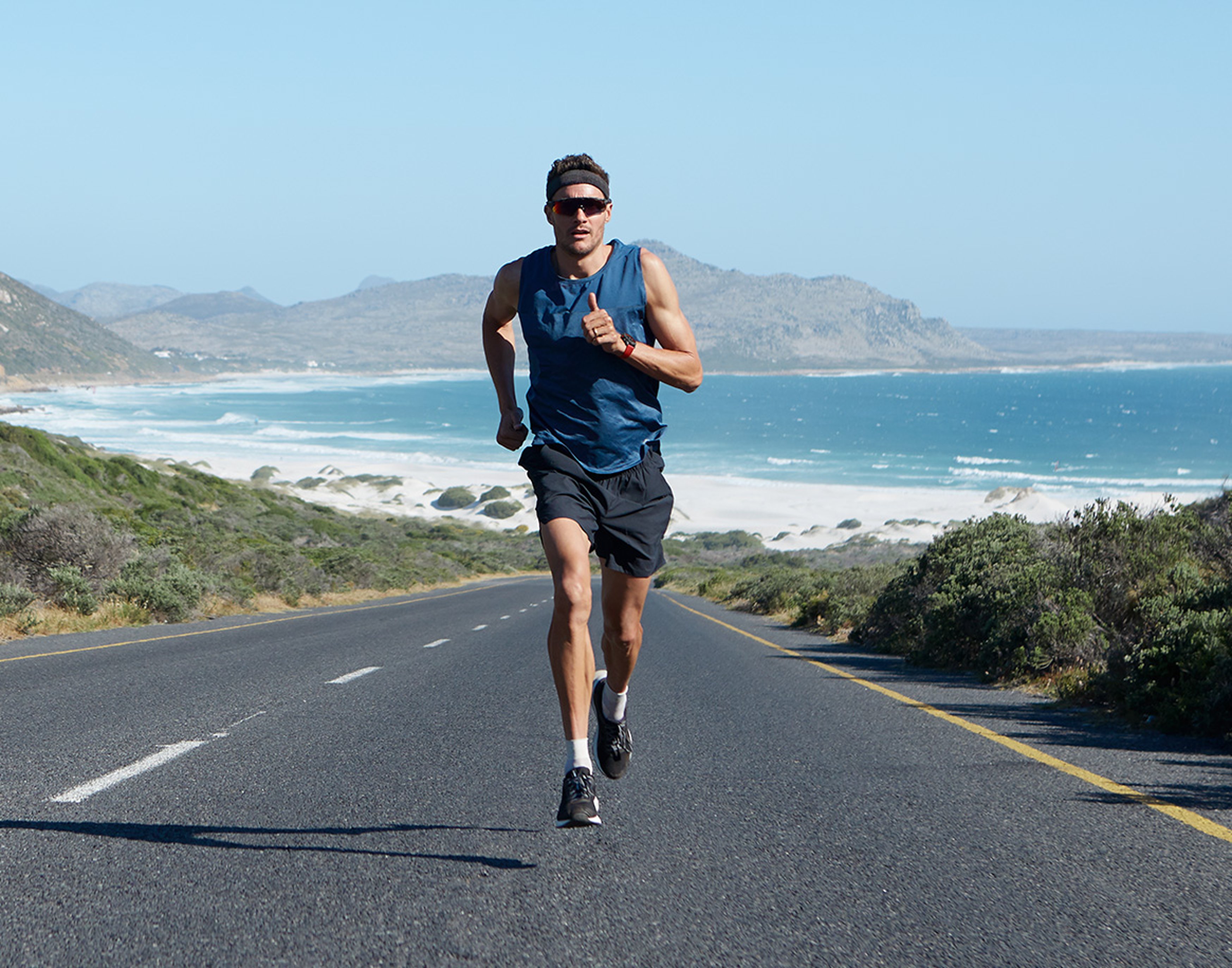 {generated} A male athlete runs along a coastal road beneath clear skies, wearing athletic gear and a Breitling watch in an active outdoor scene