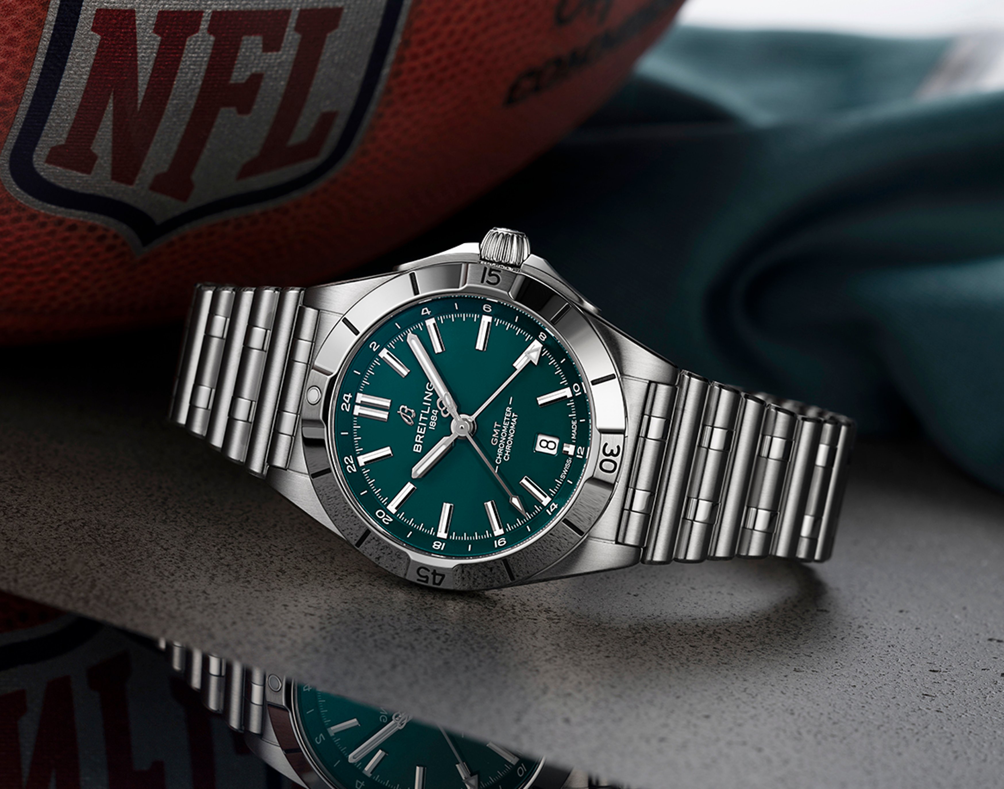 {generated} Breitling Chronomat GMT with green dial on steel bracelet set beside an NFL football in Philadelphia Eagles colors