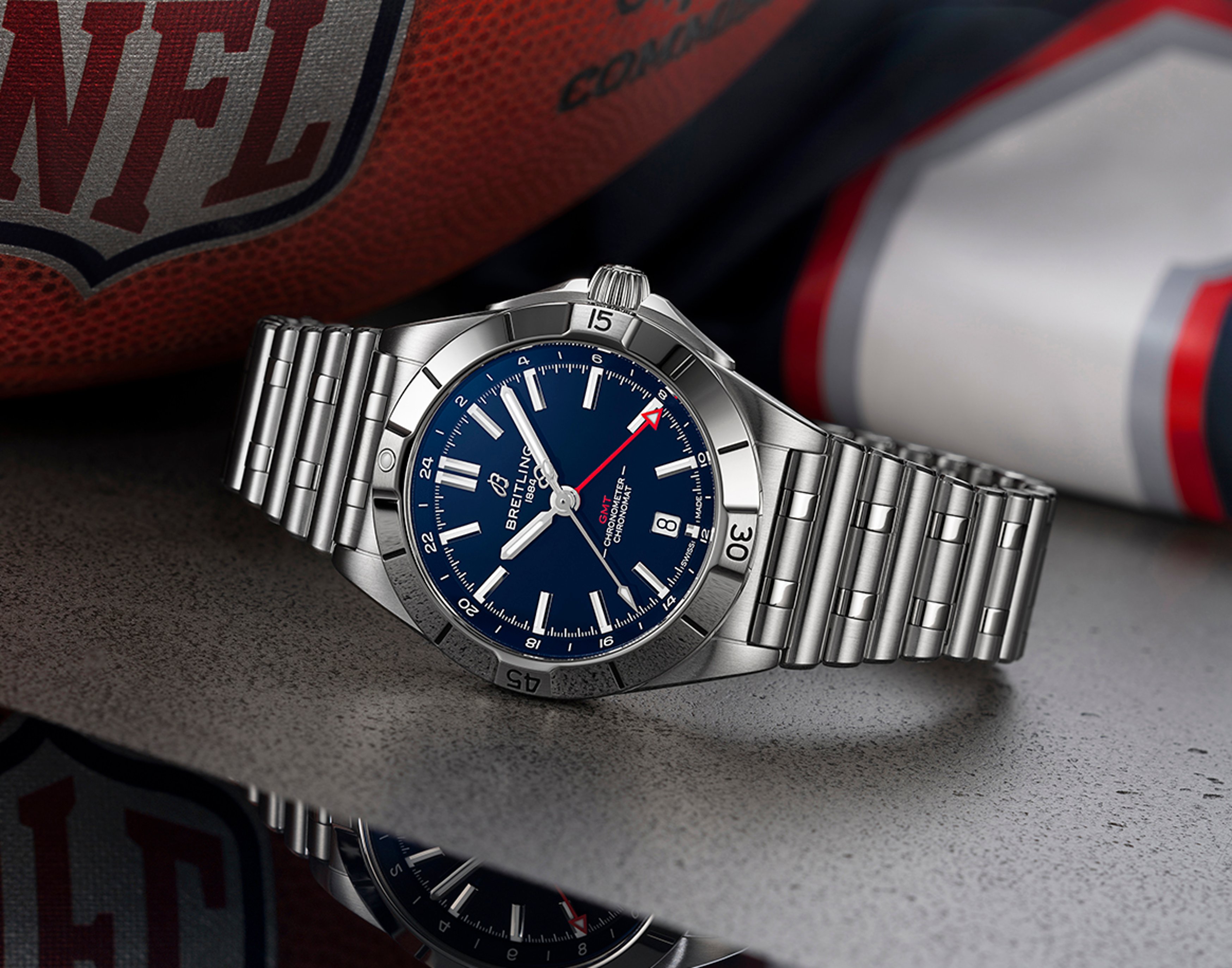 {generated} Breitling Chronomat GMT with blue dial and steel bracelet presented beside NFL gear in New England Patriots colors.