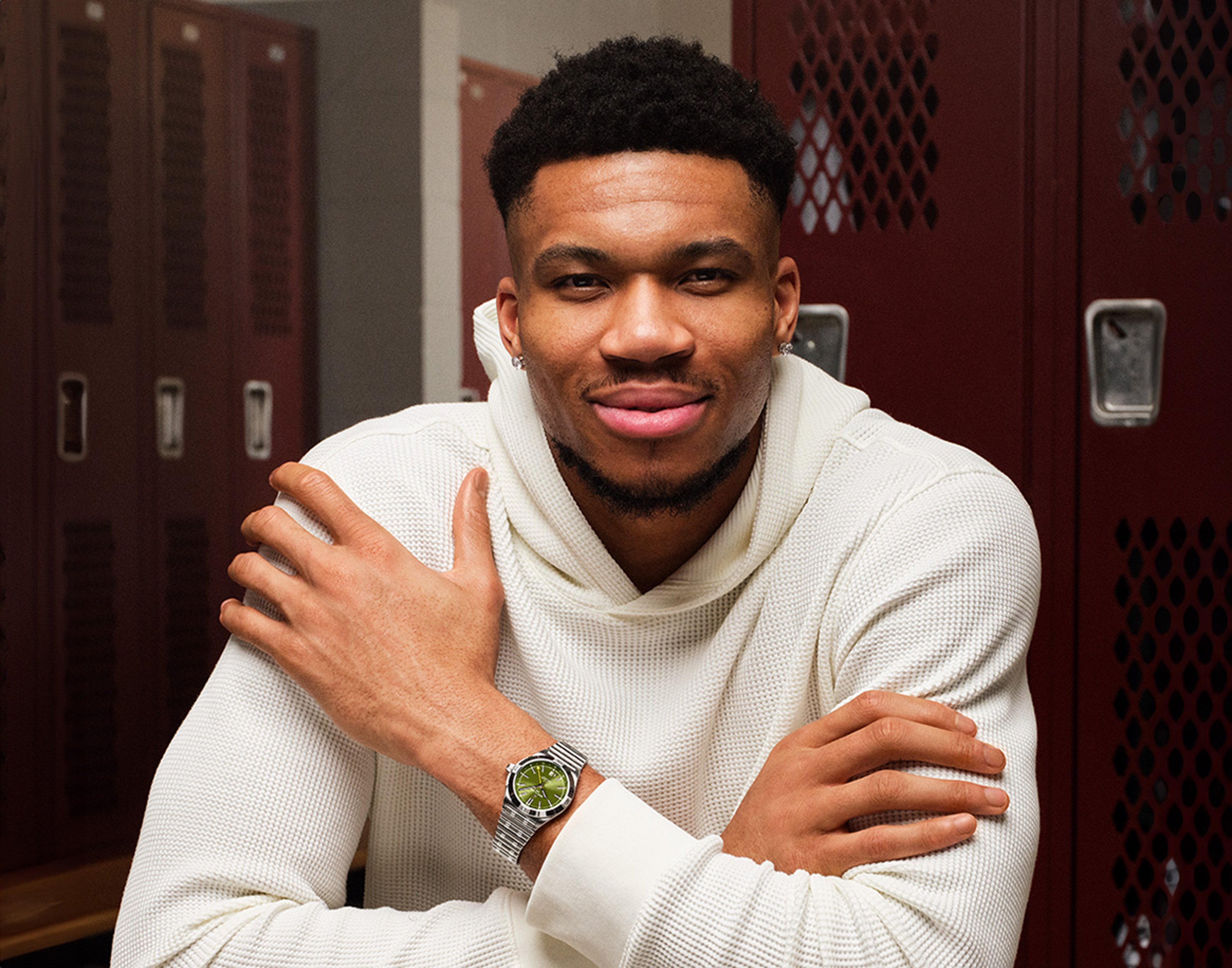 {generated} A man in a white jumper sits in a locker room wearing a Breitling watch with a green dial and steel bracelet