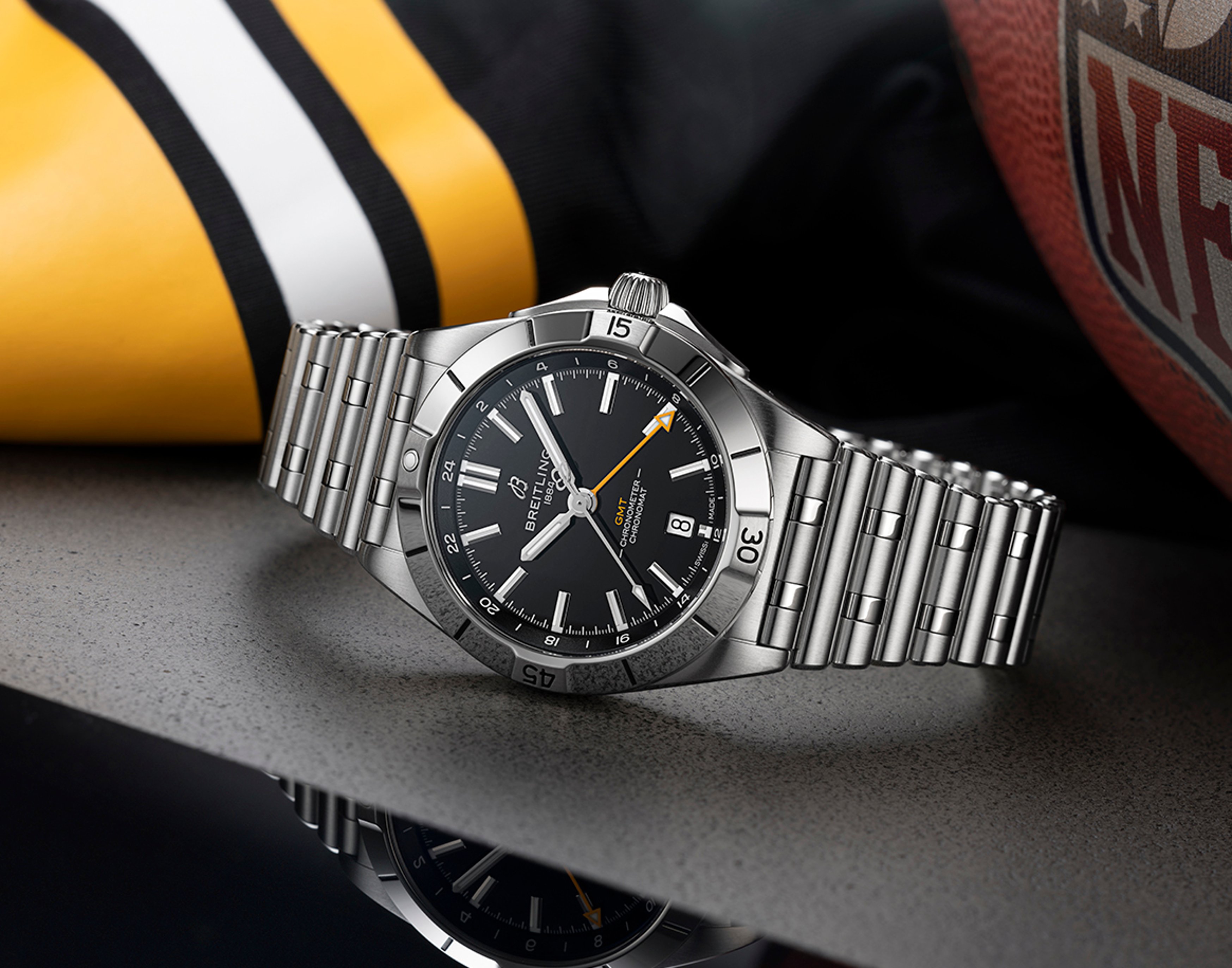 {generated} Breitling Chronomat GMT gleams on steel bracelet beside Pittsburgh Steelers gear, highlighting its bold black dial.