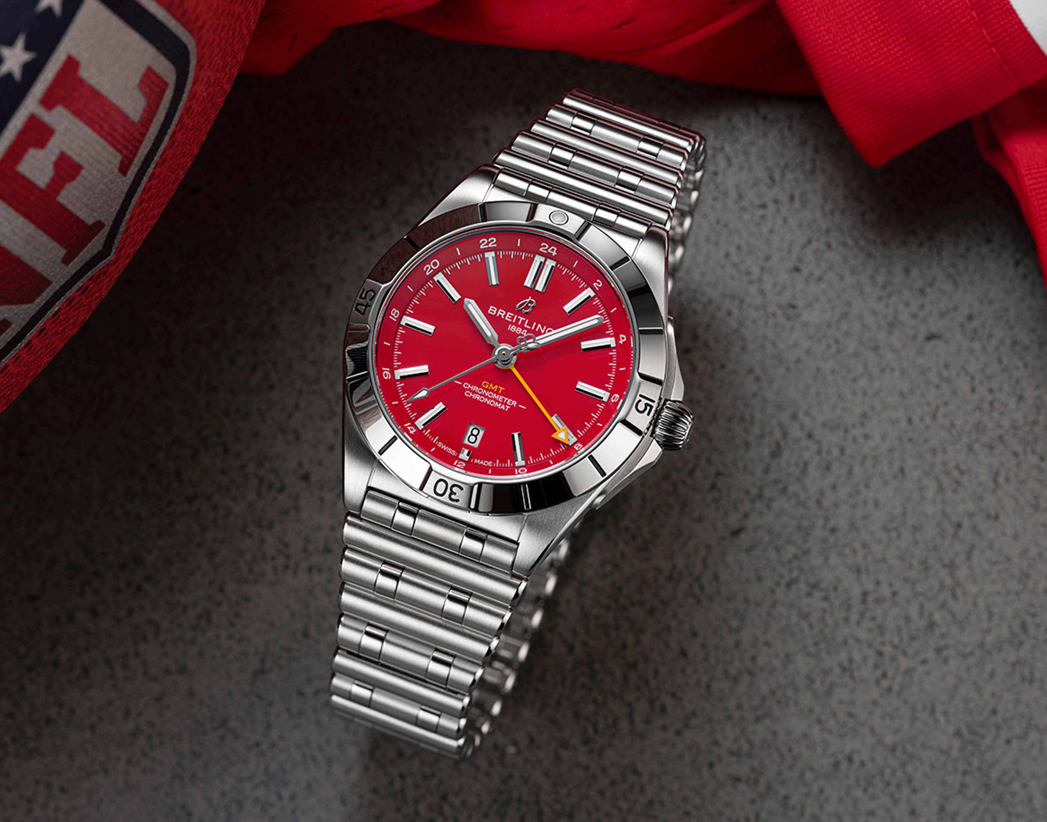 {generated} Breitling Chronomat GMT with a red Kansas City Chiefs dial shown on steel bracelet beside NFL gear on a textured surface