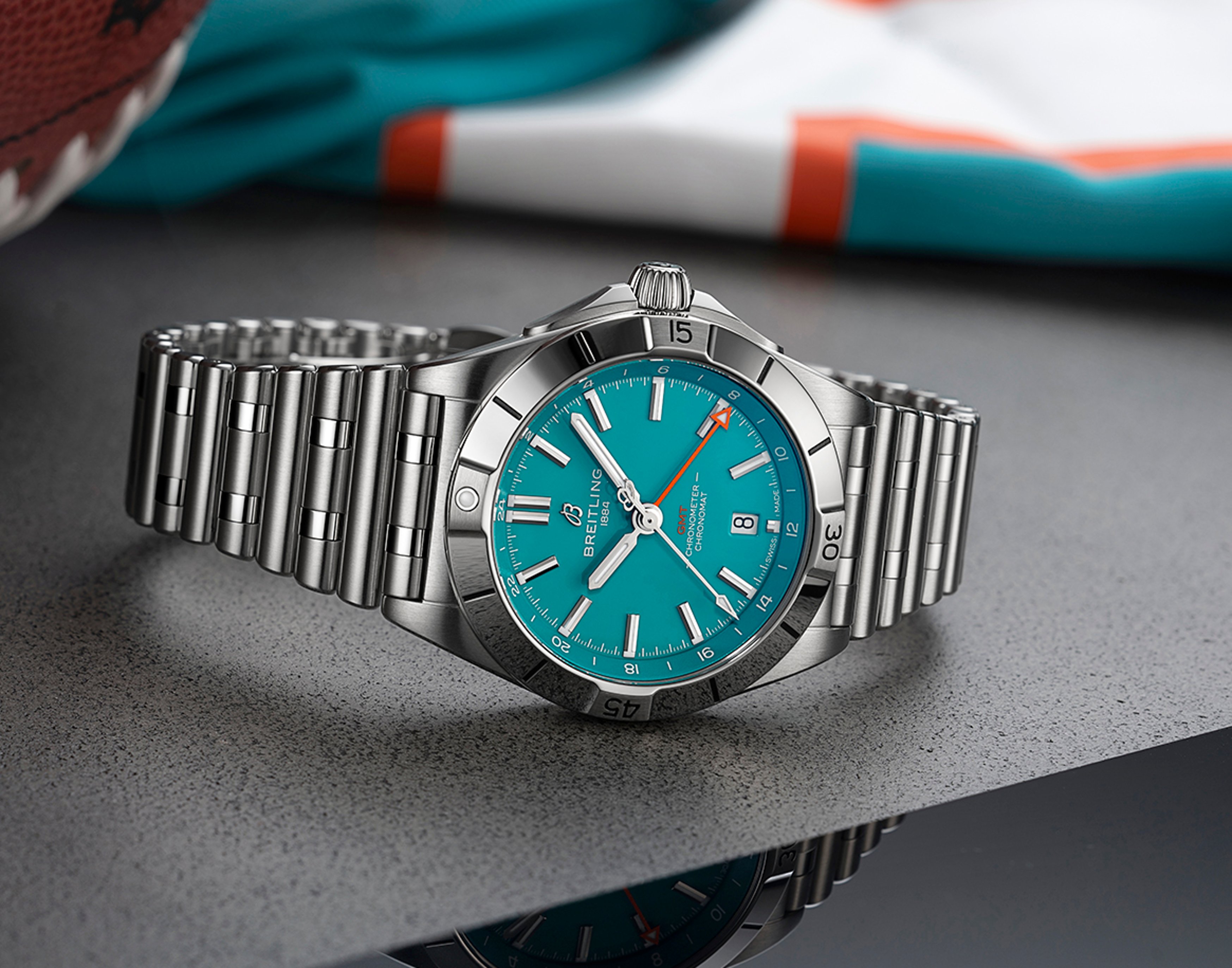 {generated} Breitling Chronomat with a turquoise dial and steel bracelet set against Miami Dolphins colors for a sporty showcase.