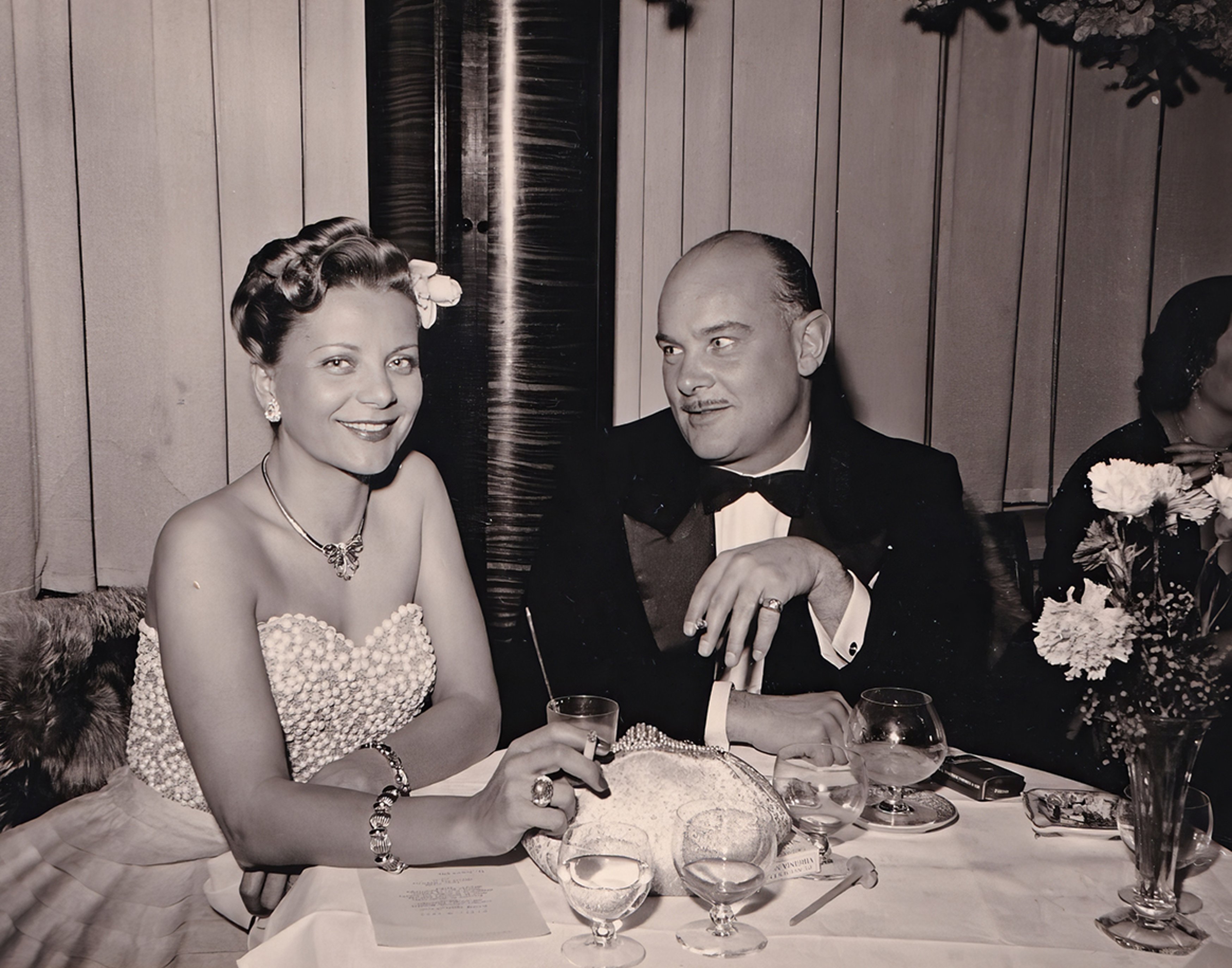 {generated} 身著復古晚禮服的優雅女士與一位男士同坐正式餐桌前，散發永恆的品味與氣質。