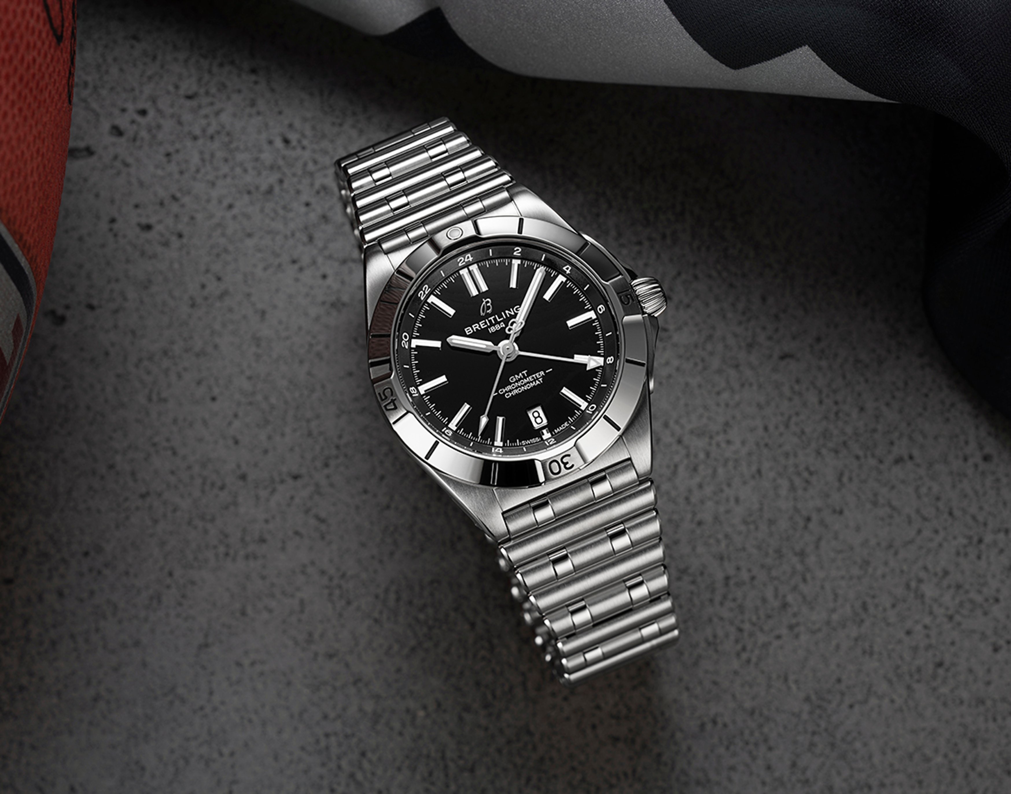 {generated} Breitling Chronomat GMT steel watch on a textured surface beside football gear, evoking the Las Vegas Raiders theme